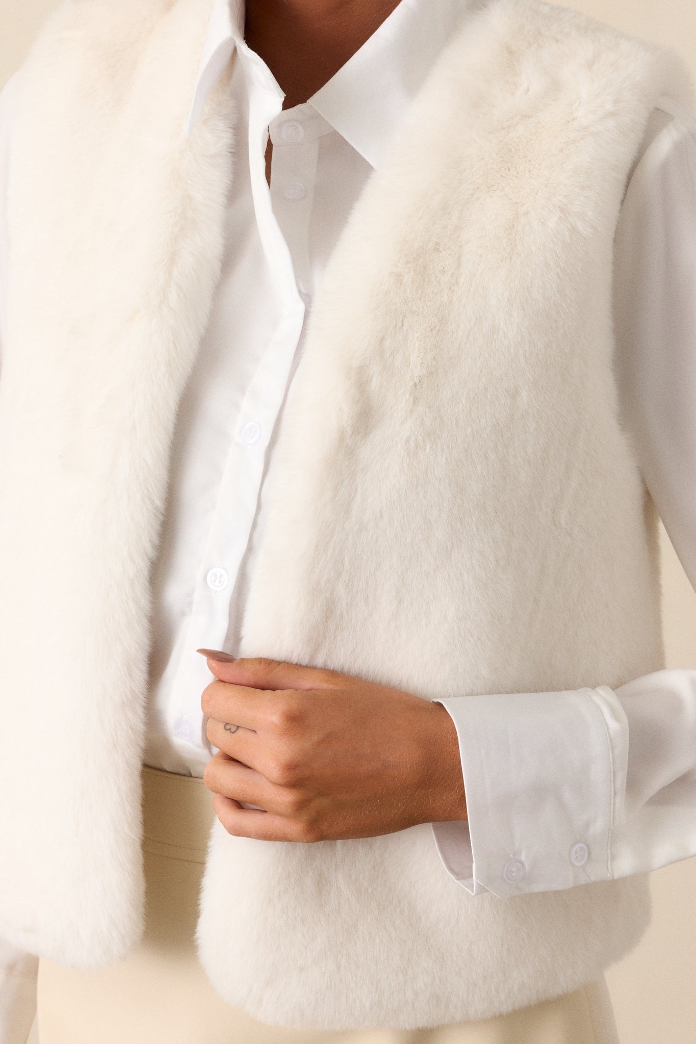 Close up view of an off white vest features an open vest design, faux fur fabric, and sleeveless cut.