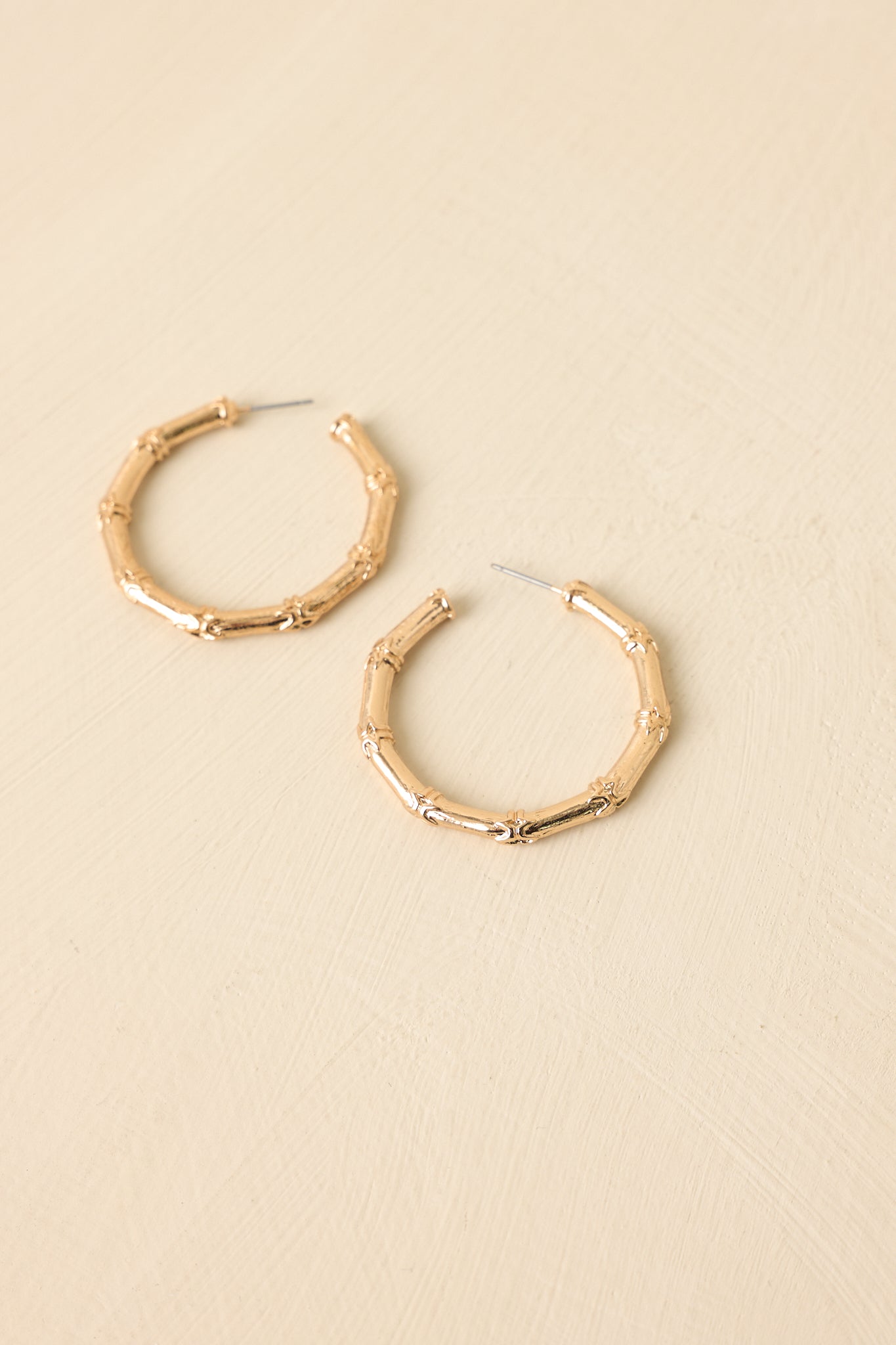 Gold bamboo-inspired hoop earrings displayed on a beige background, showcasing textured pattern and shiny finish.