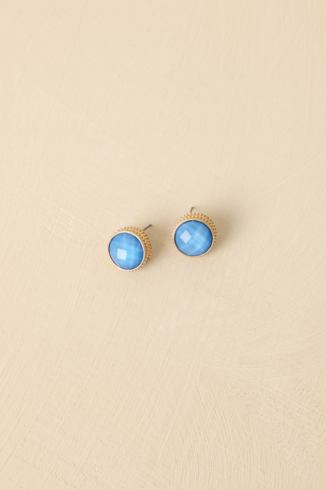 Close-up of blue stone stud earrings highlighting faceted gem, polished gold halo, and refined craftsmanship.
