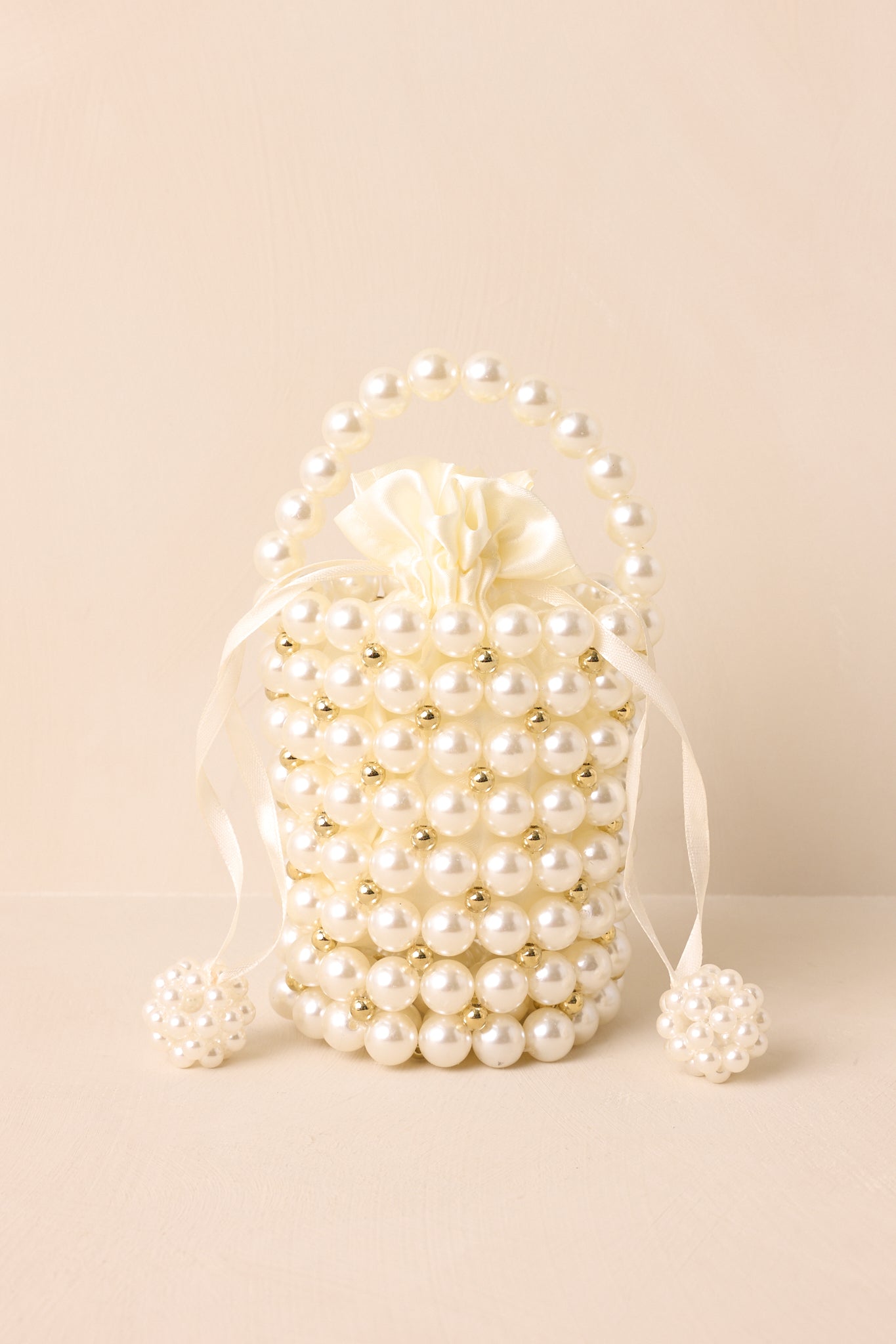 Cropped view showing the round ivory pearl charm tassels and dust bag drawstring closure.
