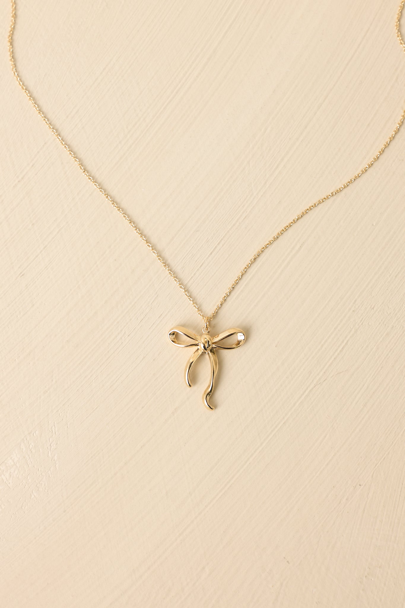Close-up of gold bow pendant necklace highlighting polished finish, graceful shape, and lightweight, wearable design.