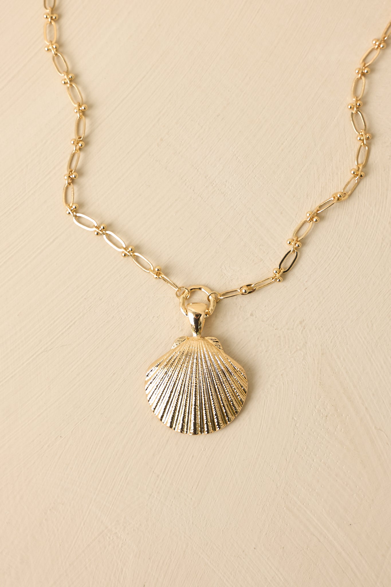 Cropped view of gold-tone chain necklace featuring elongated links and scallop shell pendant.