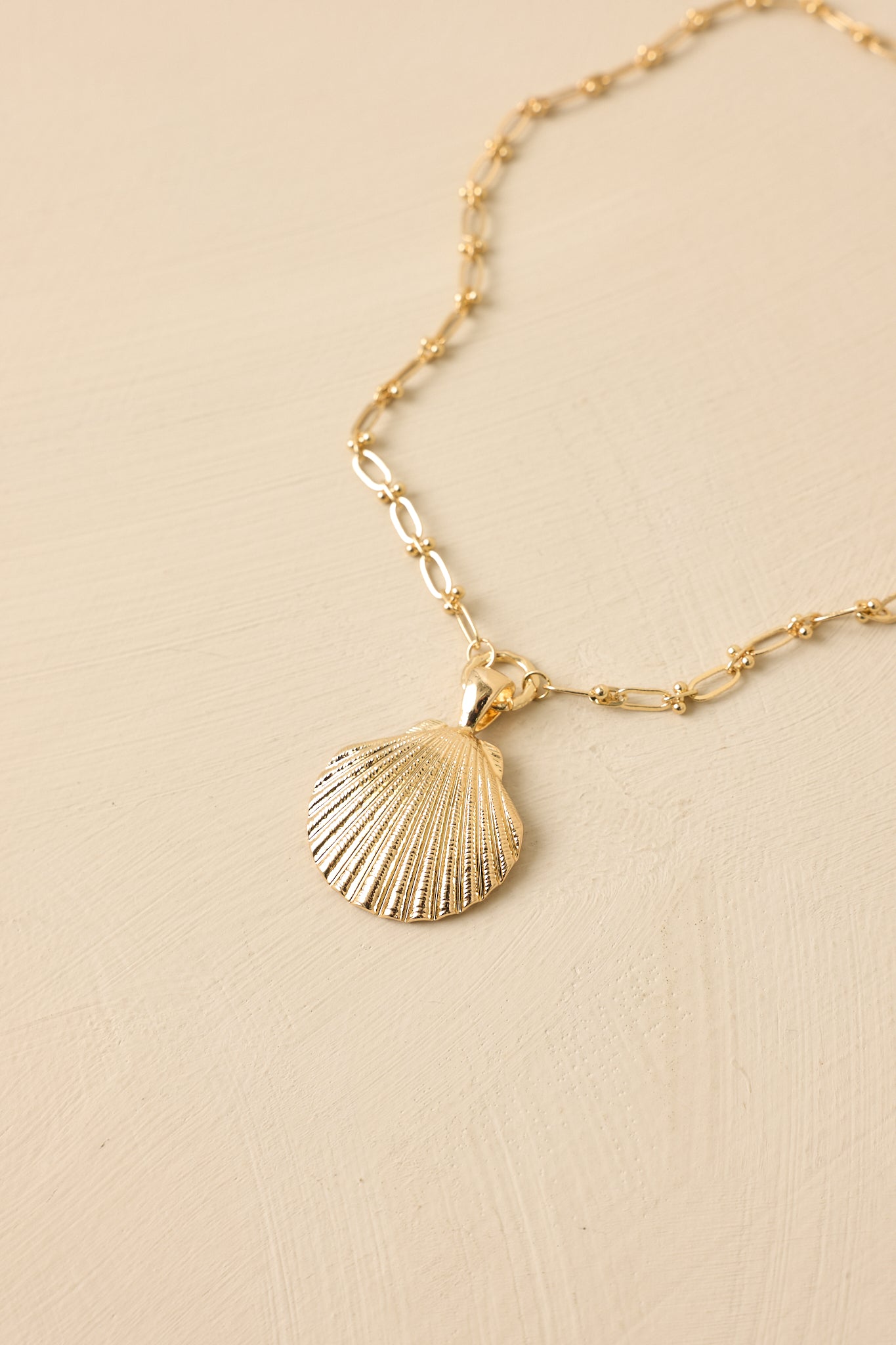 Gold-tone necklace with shell pendant displayed on beige background, showing refined chain design.
