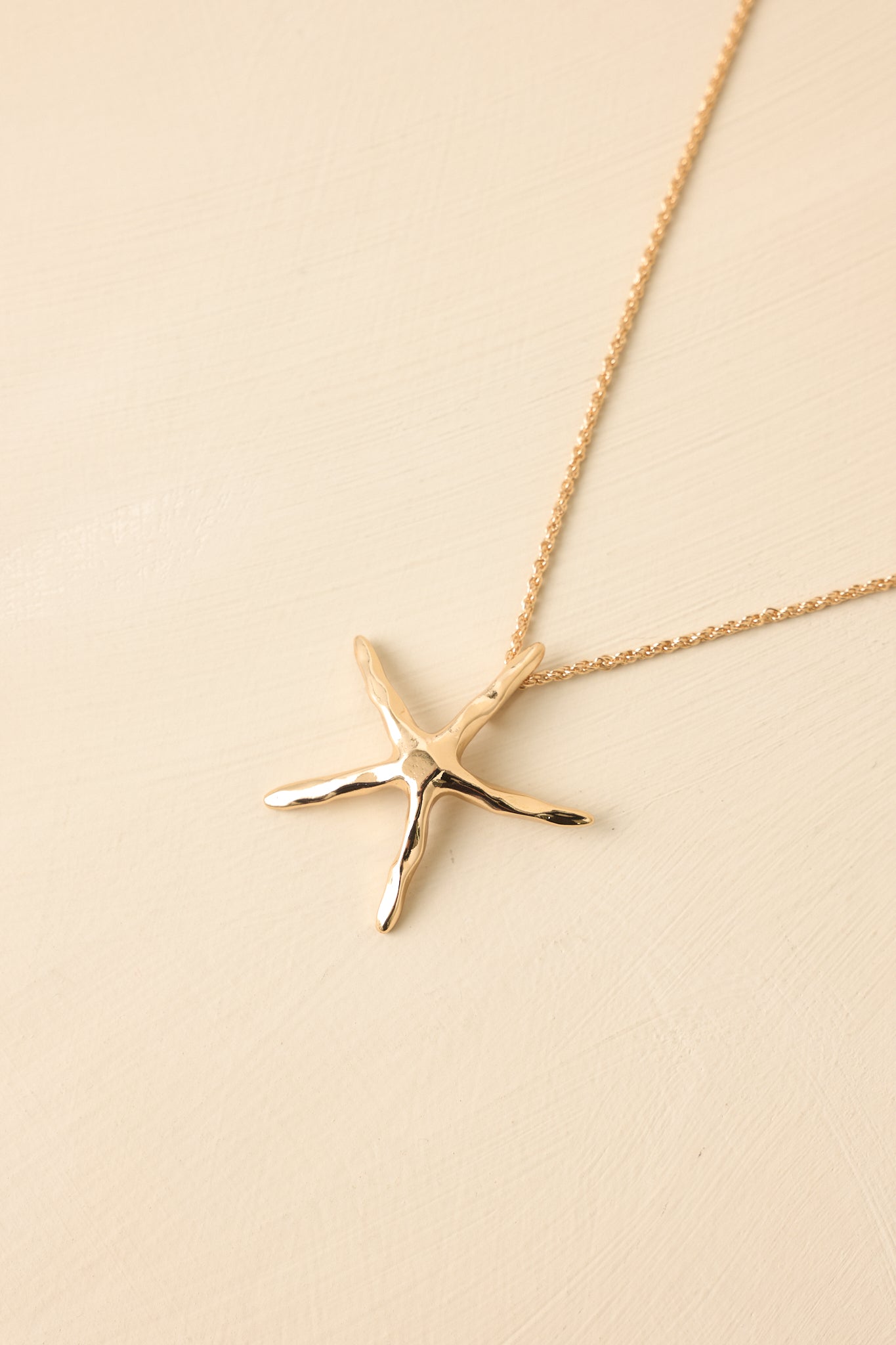 Close-up detail of gold necklace showing polished starfish pendant and luminous high-shine surface.