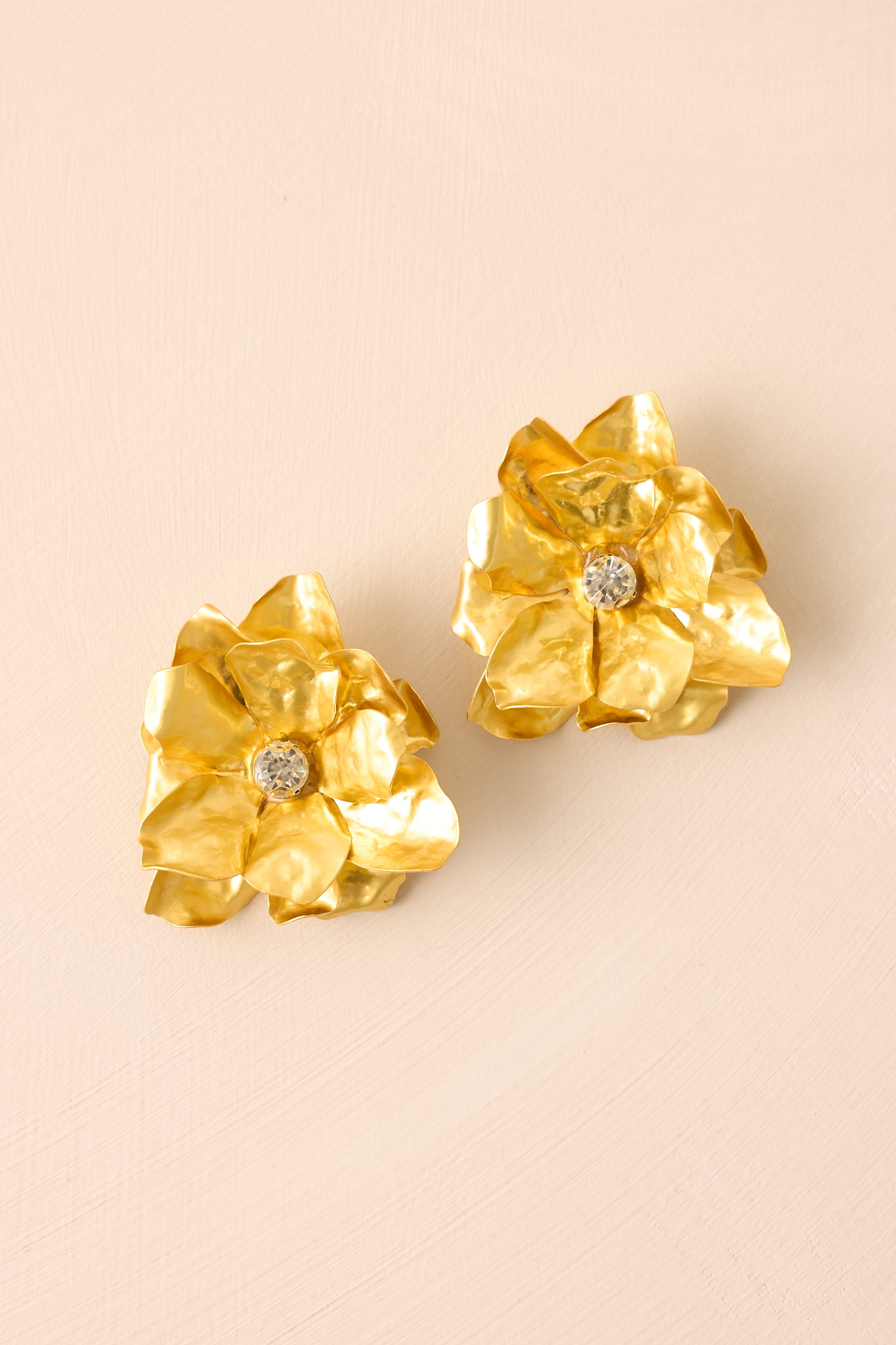 Cropped view of the gold floral earrings showcasing the large gold flower petals and clear rhinestone center.