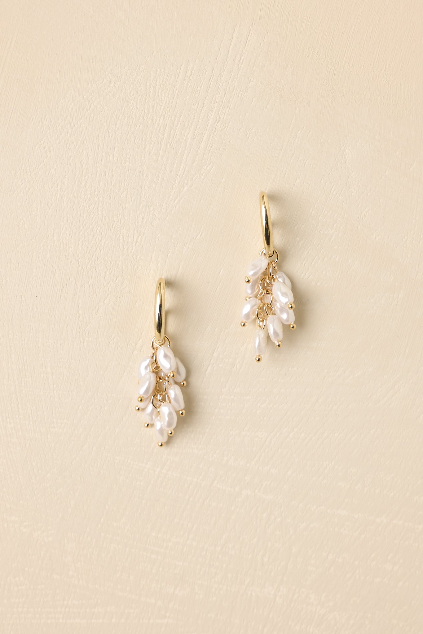 Pair of gold earrings with pearl-like beads on a beige background.