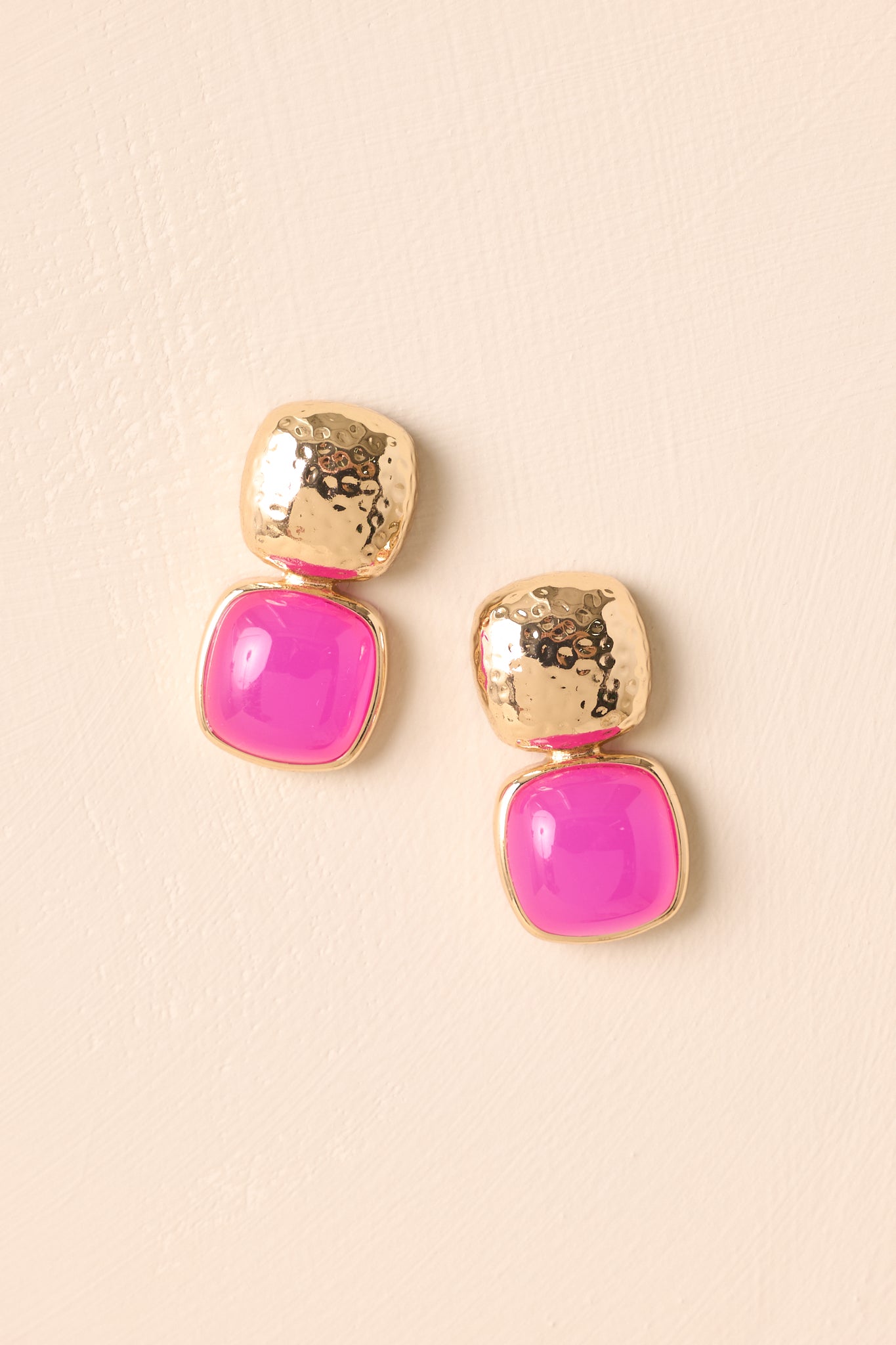 Flat-lay view of the pink earrings against a beige background, highlighting the contrast between the gold stud and the pink stone drop.