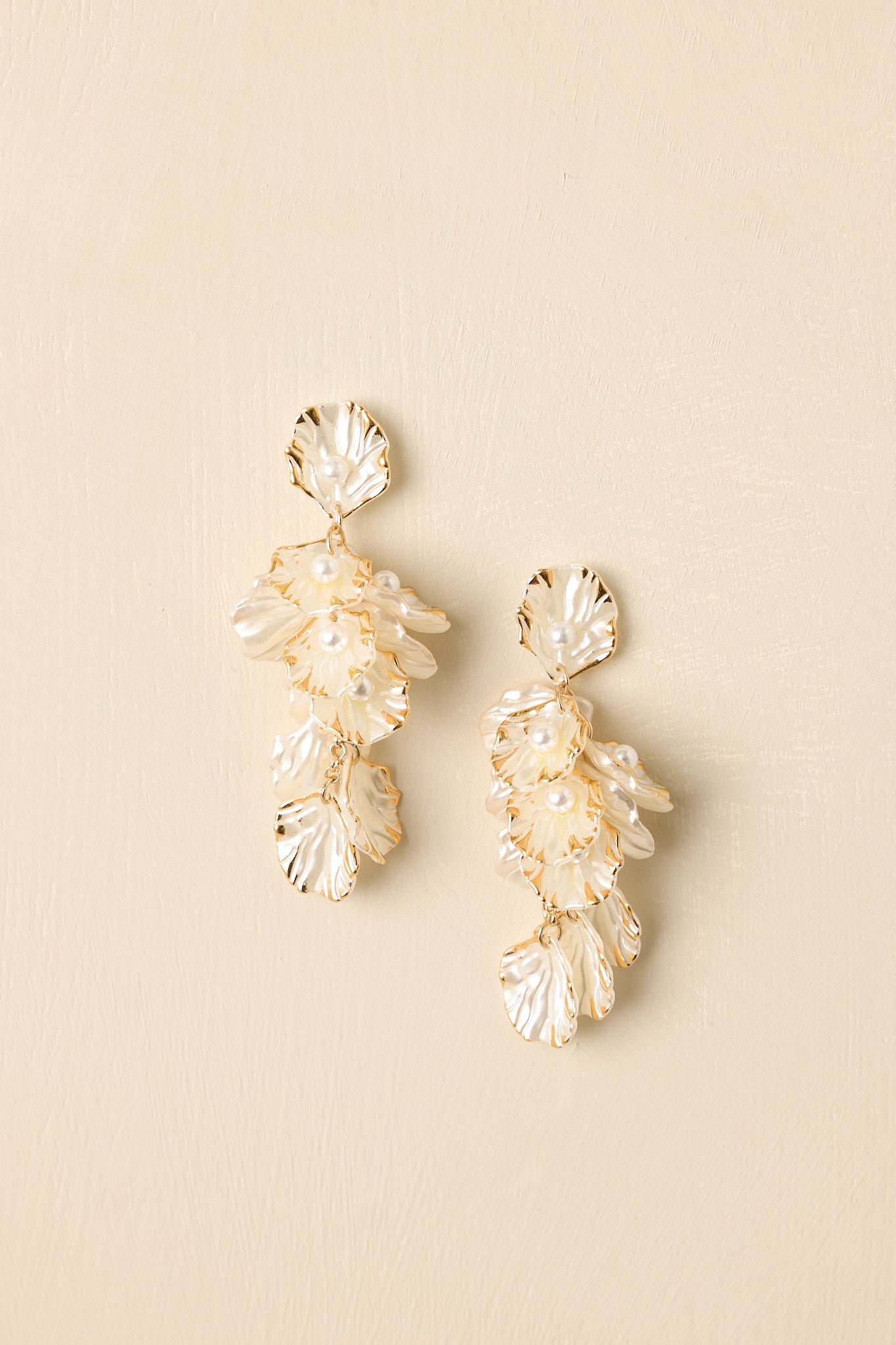 Close-up of pearlescent petal earrings with gold edging, fine chain links, and delicate pearl accents showing intricate texture.