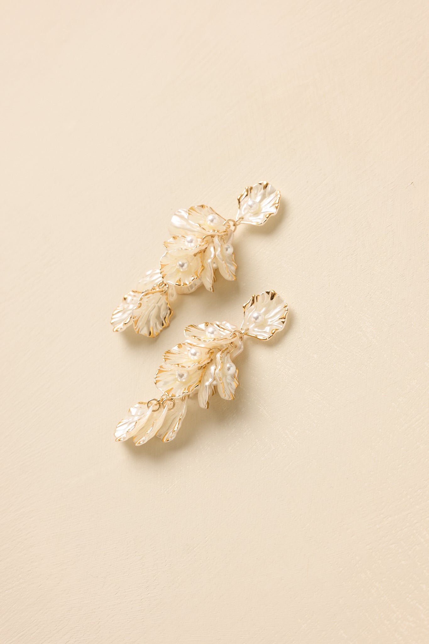 Pearlescent shell-inspired drop earrings with gold trim and cascading chains displayed on a beige background.