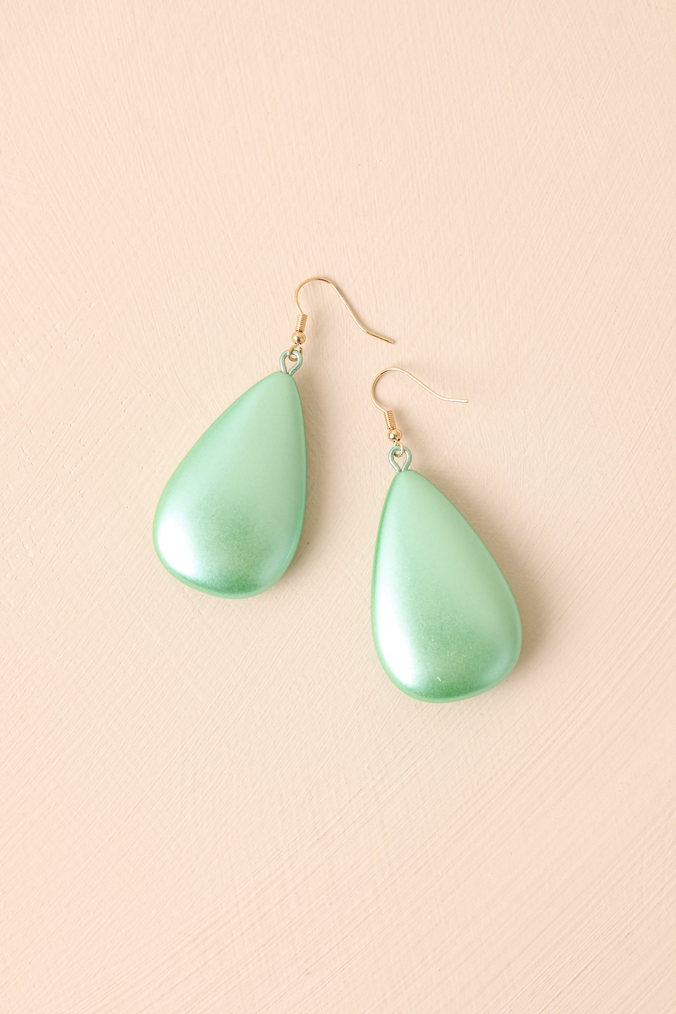 Flat-lay view of the mint earrings placed against a beige background, highlighting the pearlescent mint green oval and gold hardware.