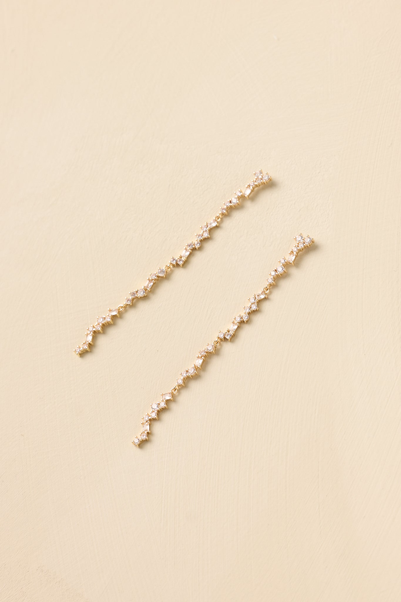 Close-up of gold linear earrings showcasing faceted crystals aligned in a delicate vertical strand with refined shine.