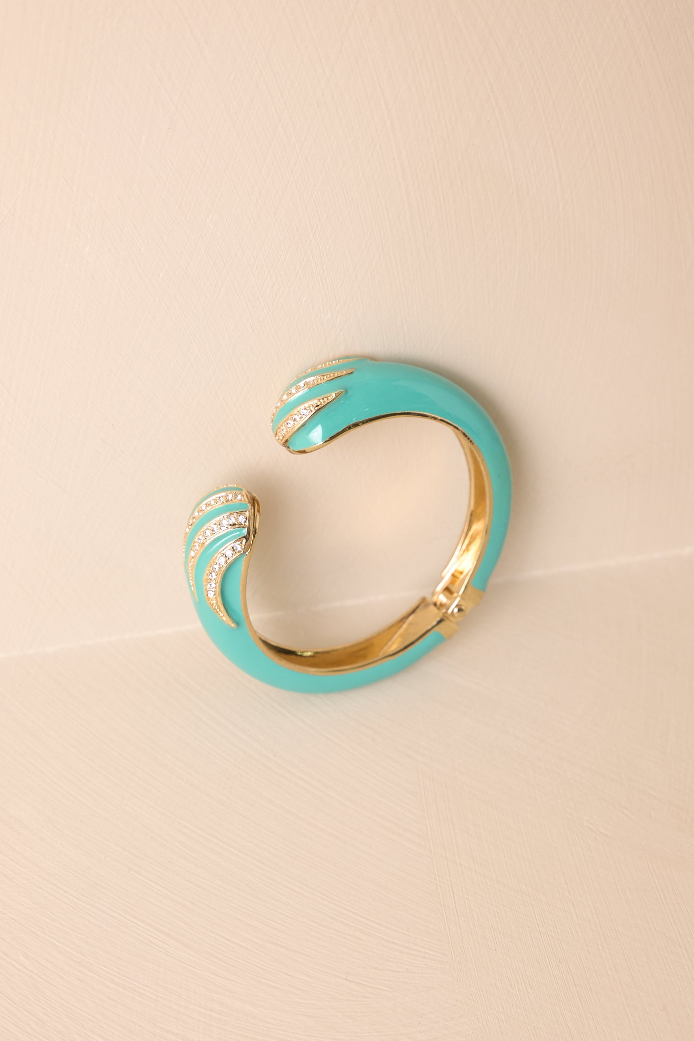 Turquoise open cuff bracelet displayed on a beige background, showcasing both rhinestone-embellished ends and the polished gold hinge.