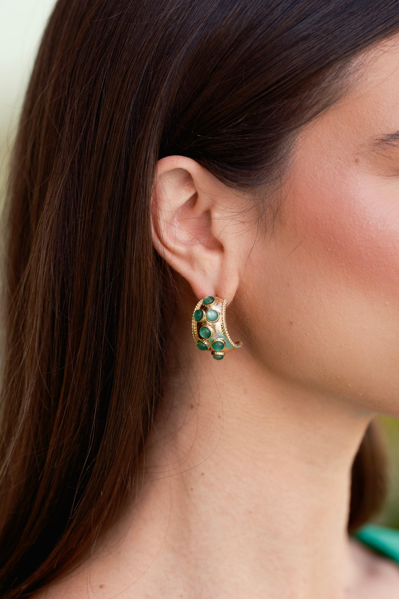 Cropped front view of the earrings showing the worn gold-colored base with bezel set green stones and incomplete hoop design.