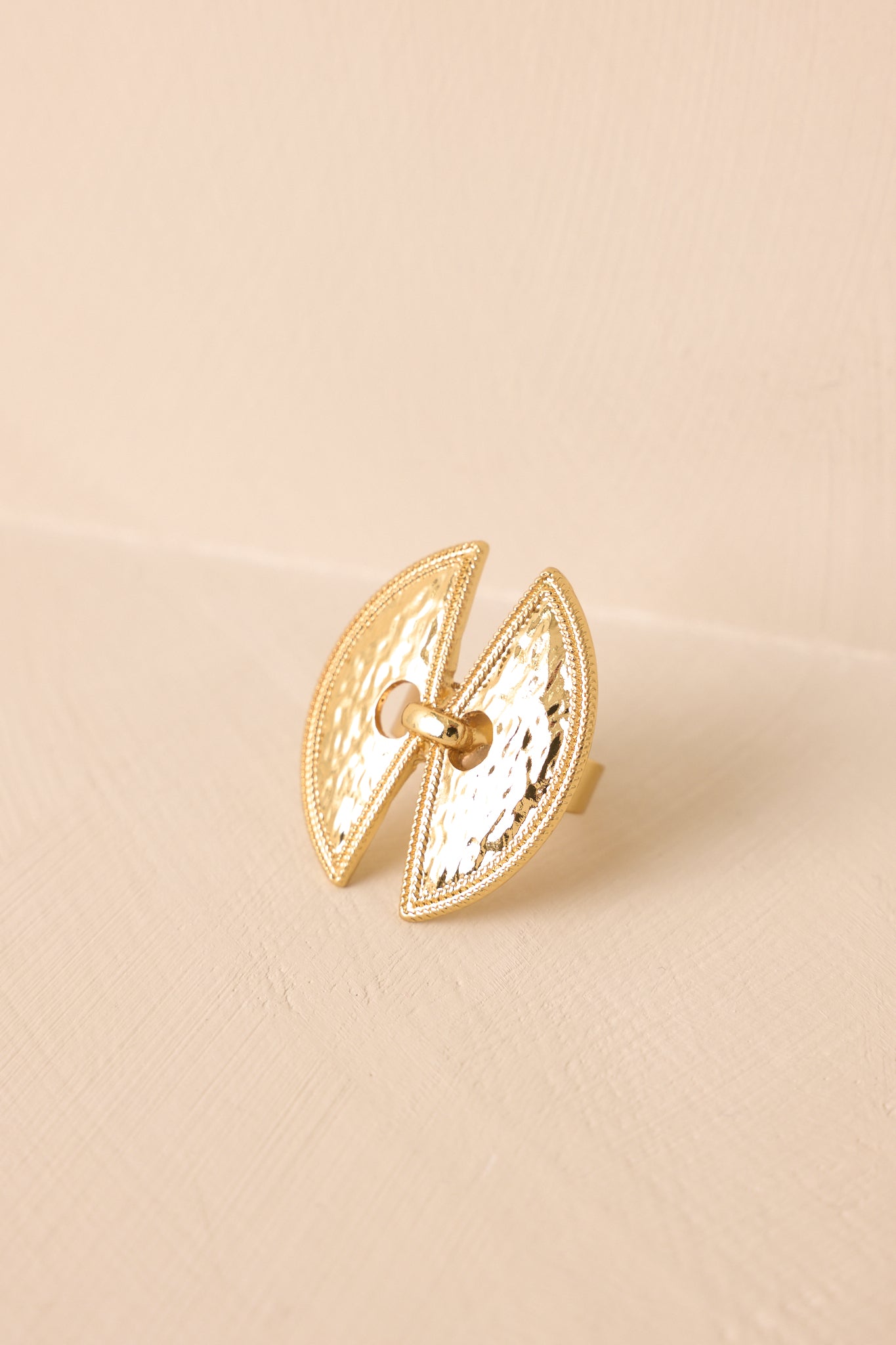 Full view of the hammered gold ring on a beige background, displaying the open double marquise shape and adjustable band.