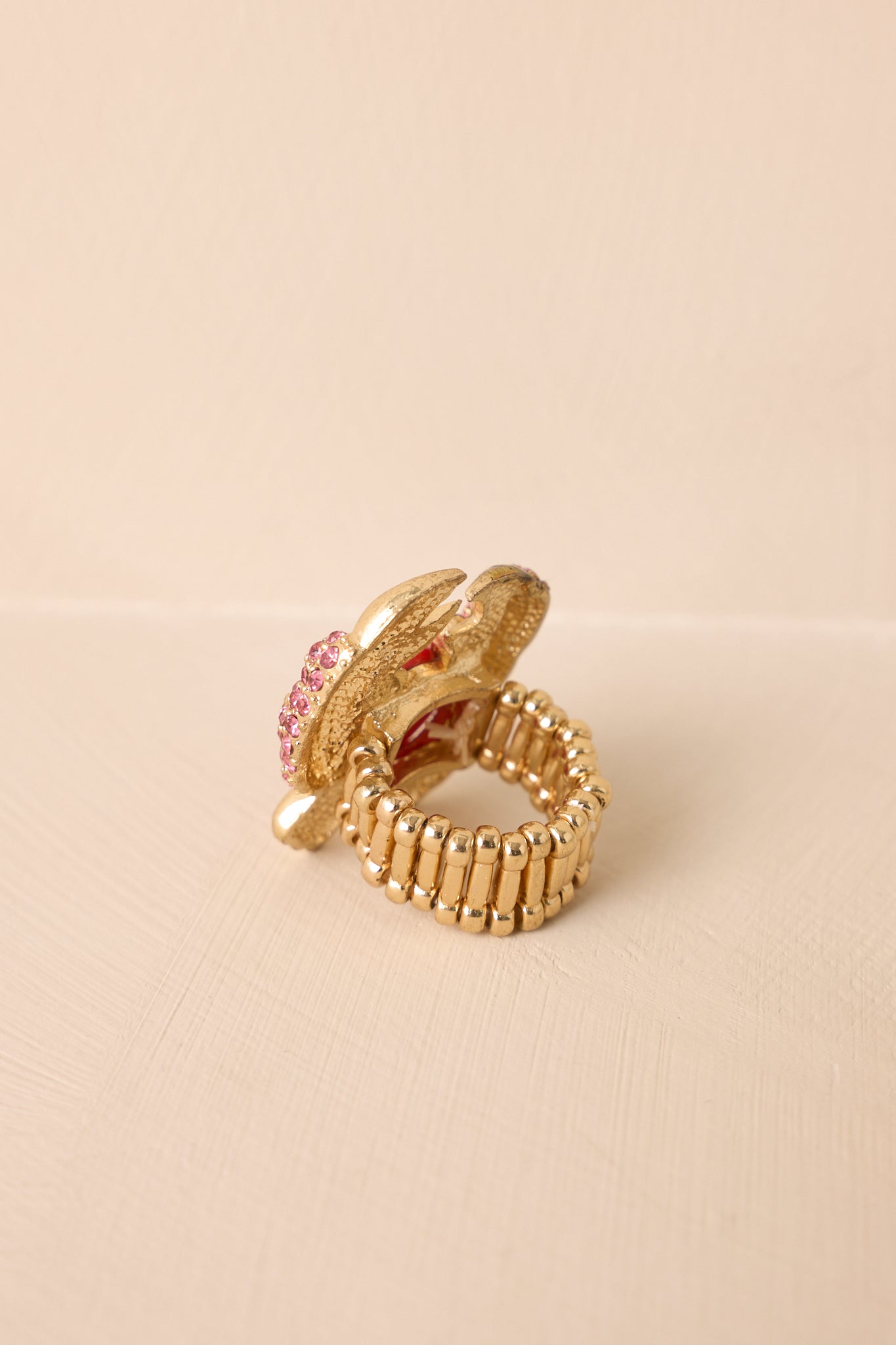 Partial view of the gold ring showing the beaded stretchy band and one claw of the crab pendant adorned with small pink rhinestones.
