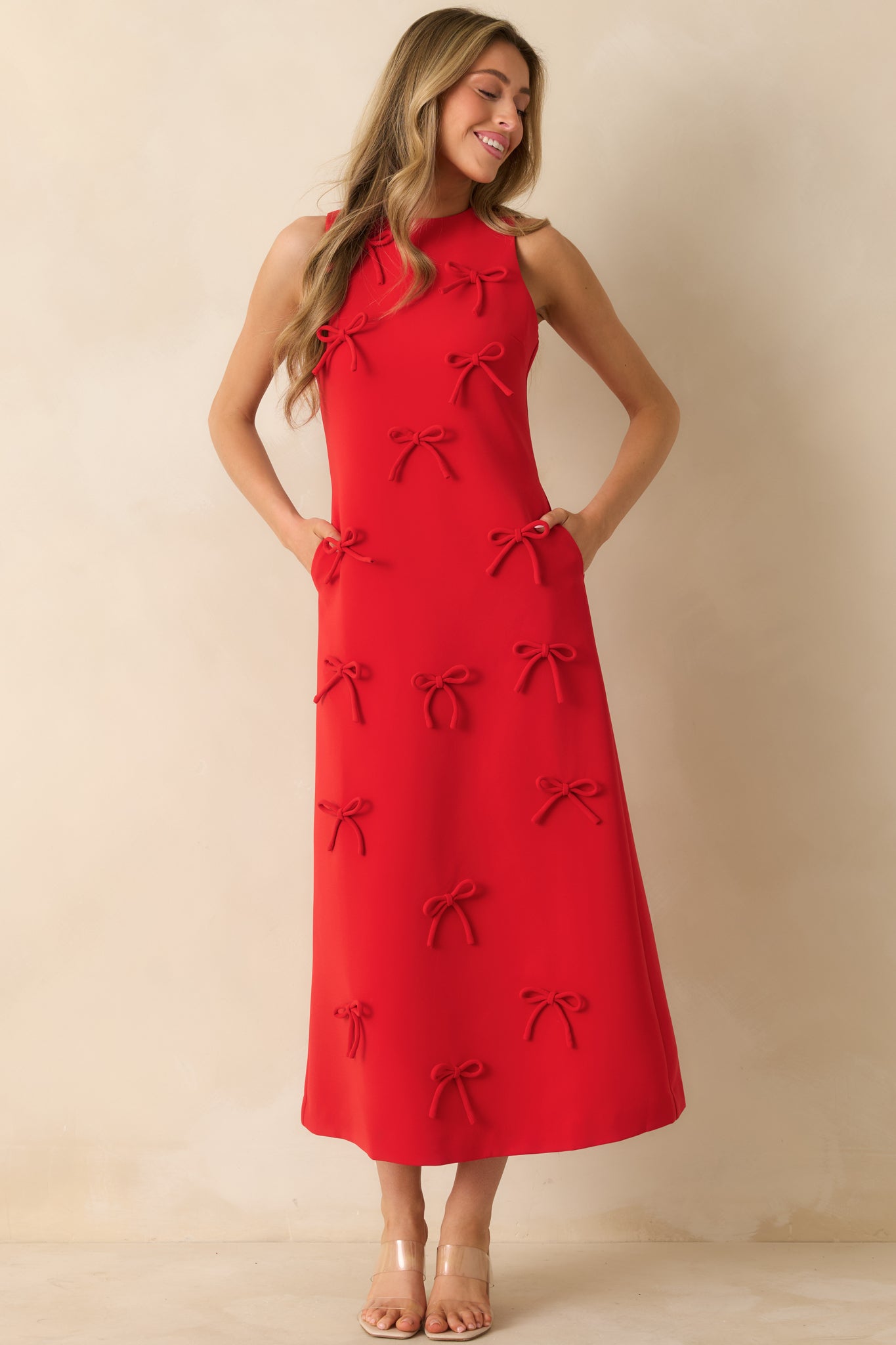 Red sleeveless maxi dress with a straight silhouette and bow appliqués, featuring a crew neckline and side pockets.