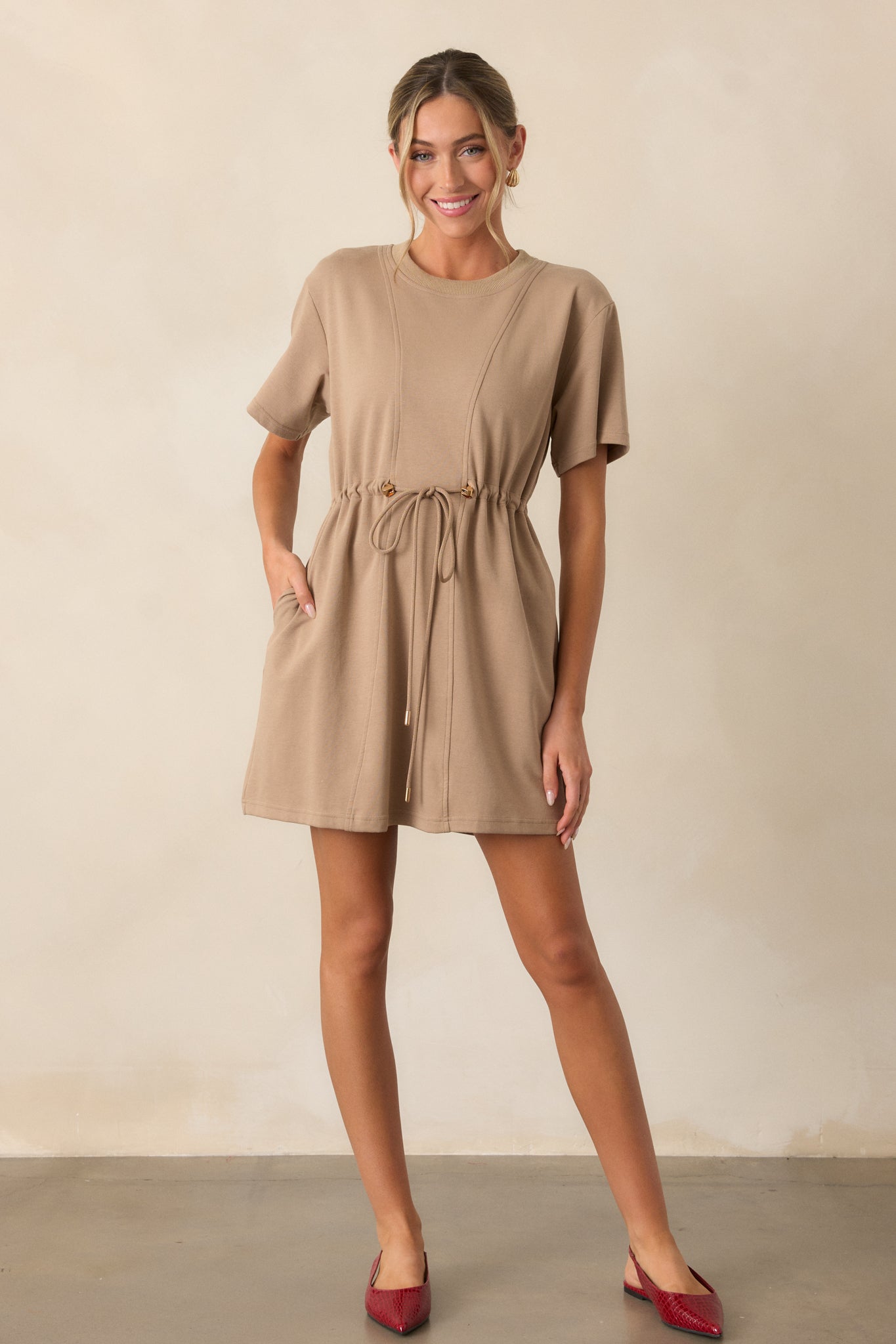 Front-facing full view of the light mocha mini dress highlighting the soft fabric and gold accents on the drawstring waist and aglets.