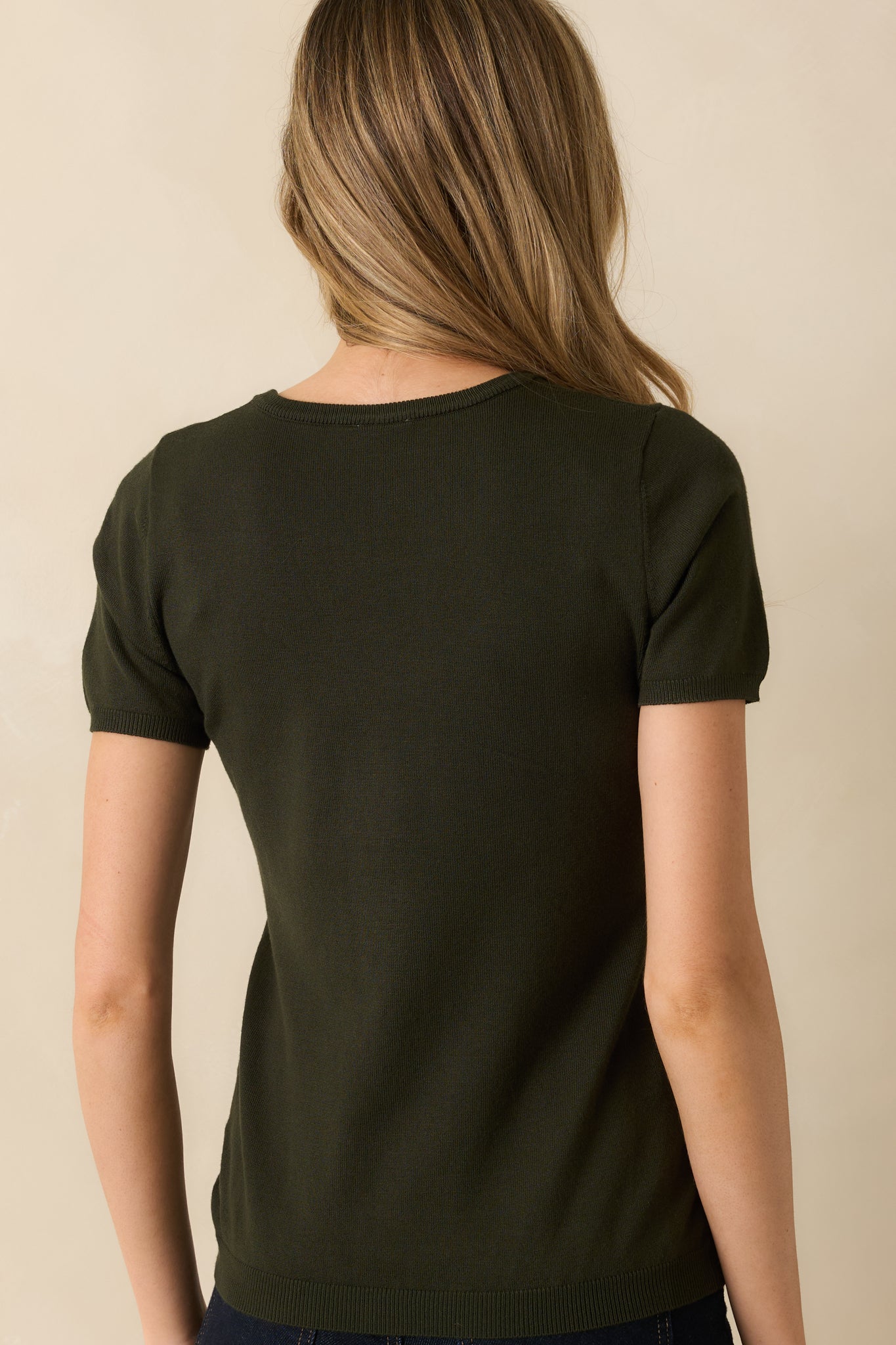 Rear view of the dark green sweater top highlighting the smooth knit fabric and simple ribbed hem.