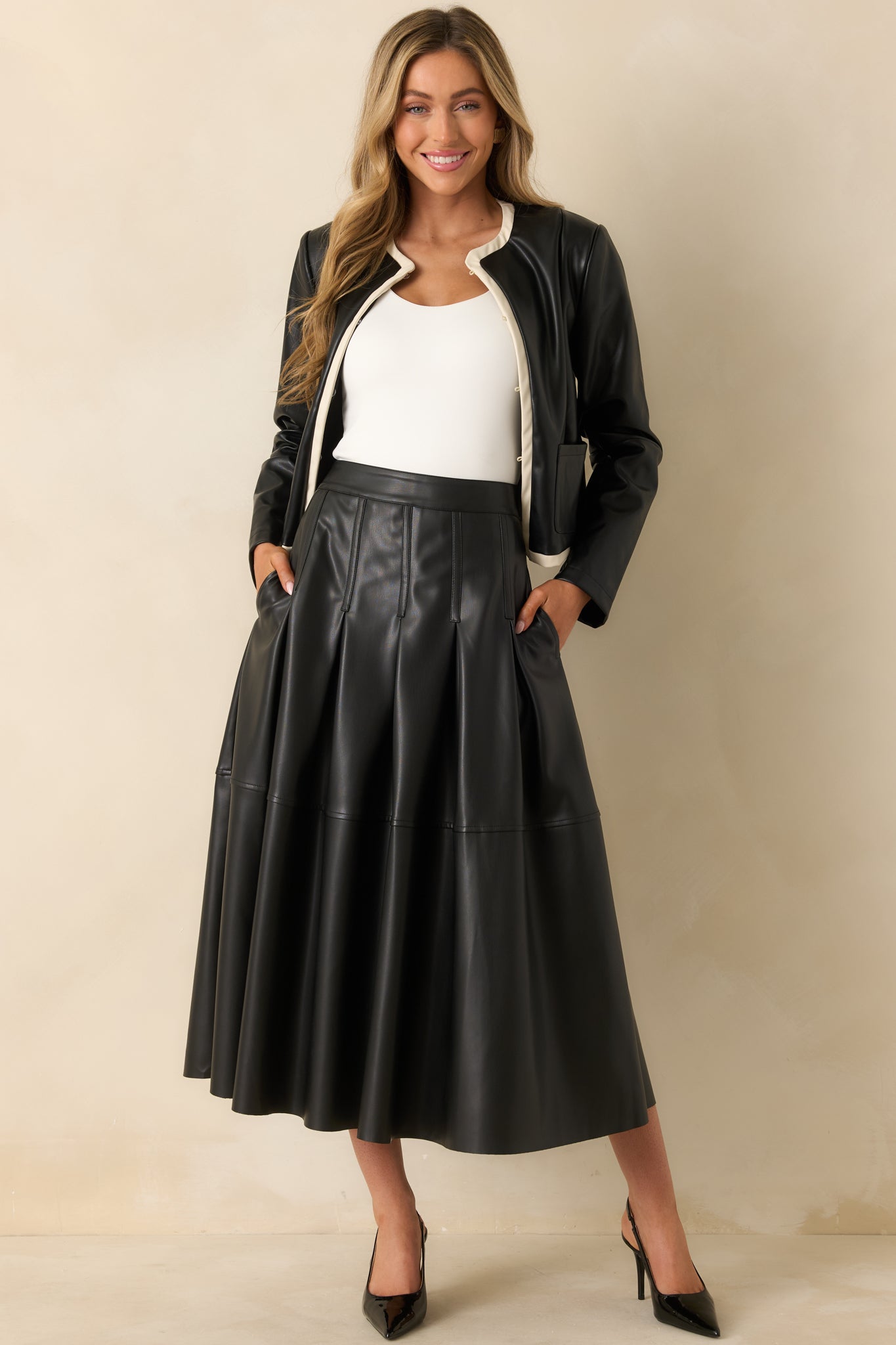 Full A-line skirt in black faux leather featuring fluid movement and tailored pleating at the waist.