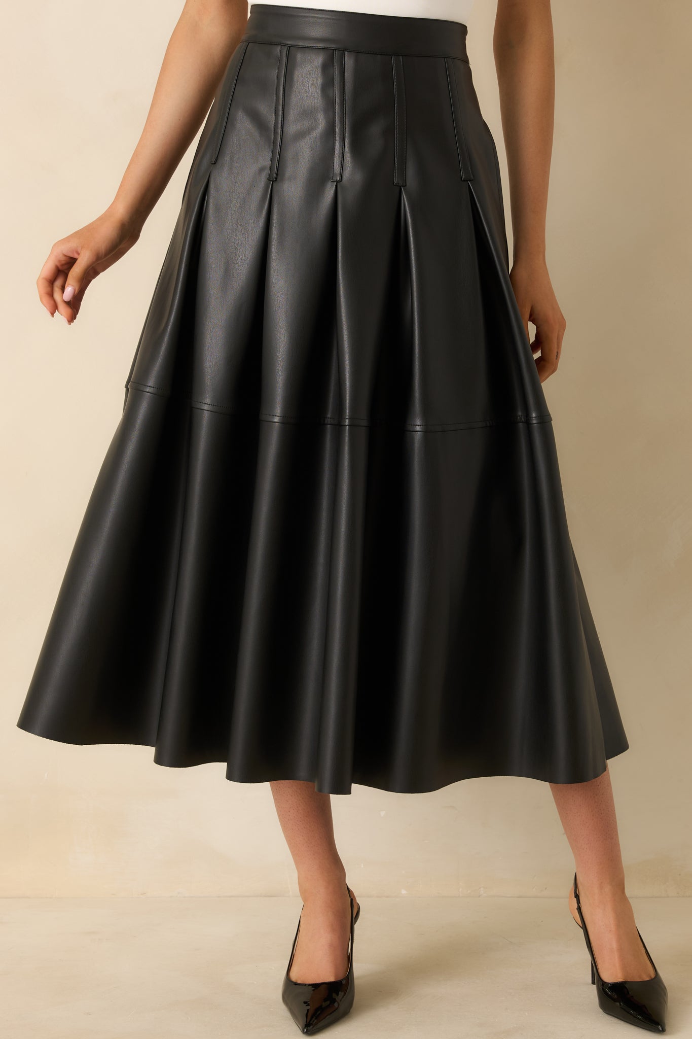 Black faux leather midi skirt with structured vertical pleats and a smooth fitted waistband.