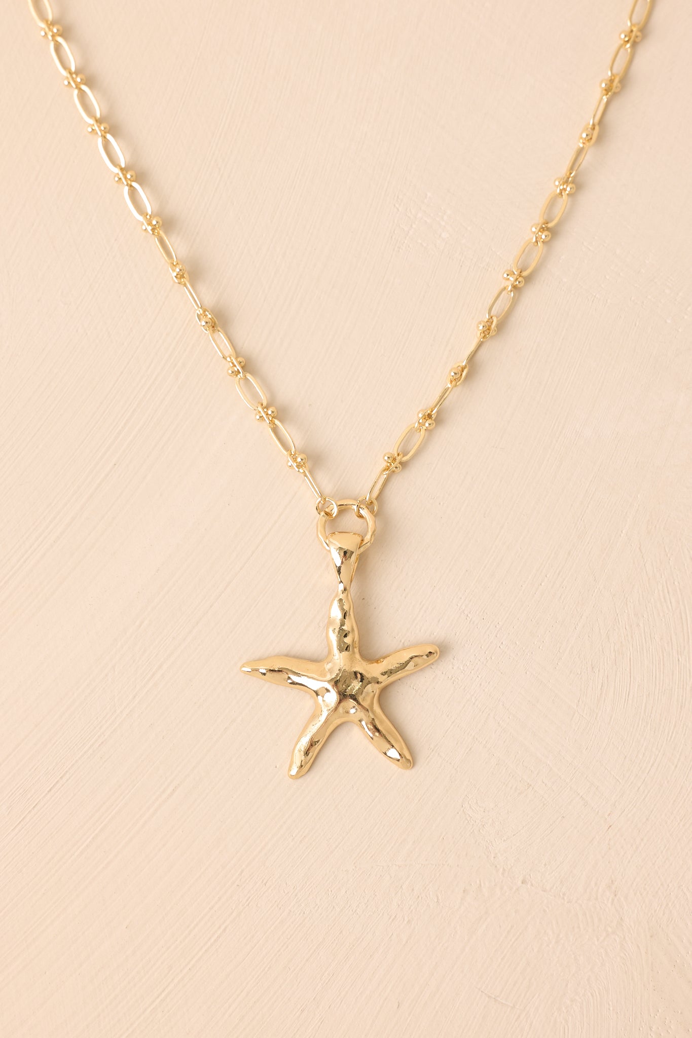 Extreme close-up of the necklace's chain, focusing on the intricate gold beading and smooth finish of the starfish pendant.