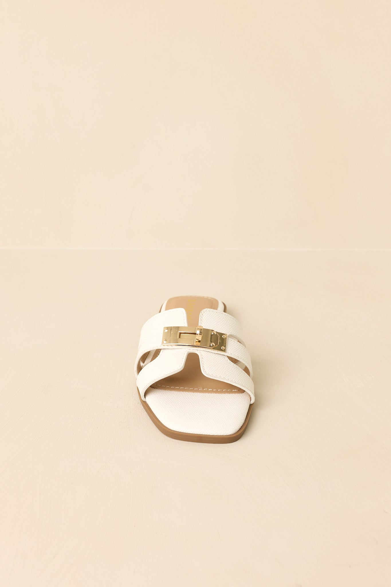 Front view of white faux leather slides against a beige background emphasizing layered strap design.