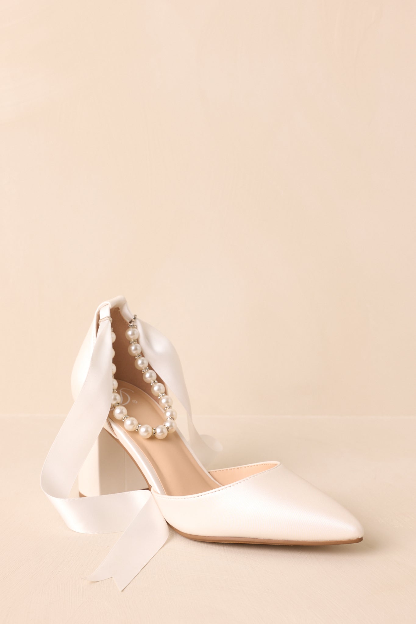 A detailed side profile highlighting the ivory faux pearl and rhinestone ankle strap which would wrap around the ankle.