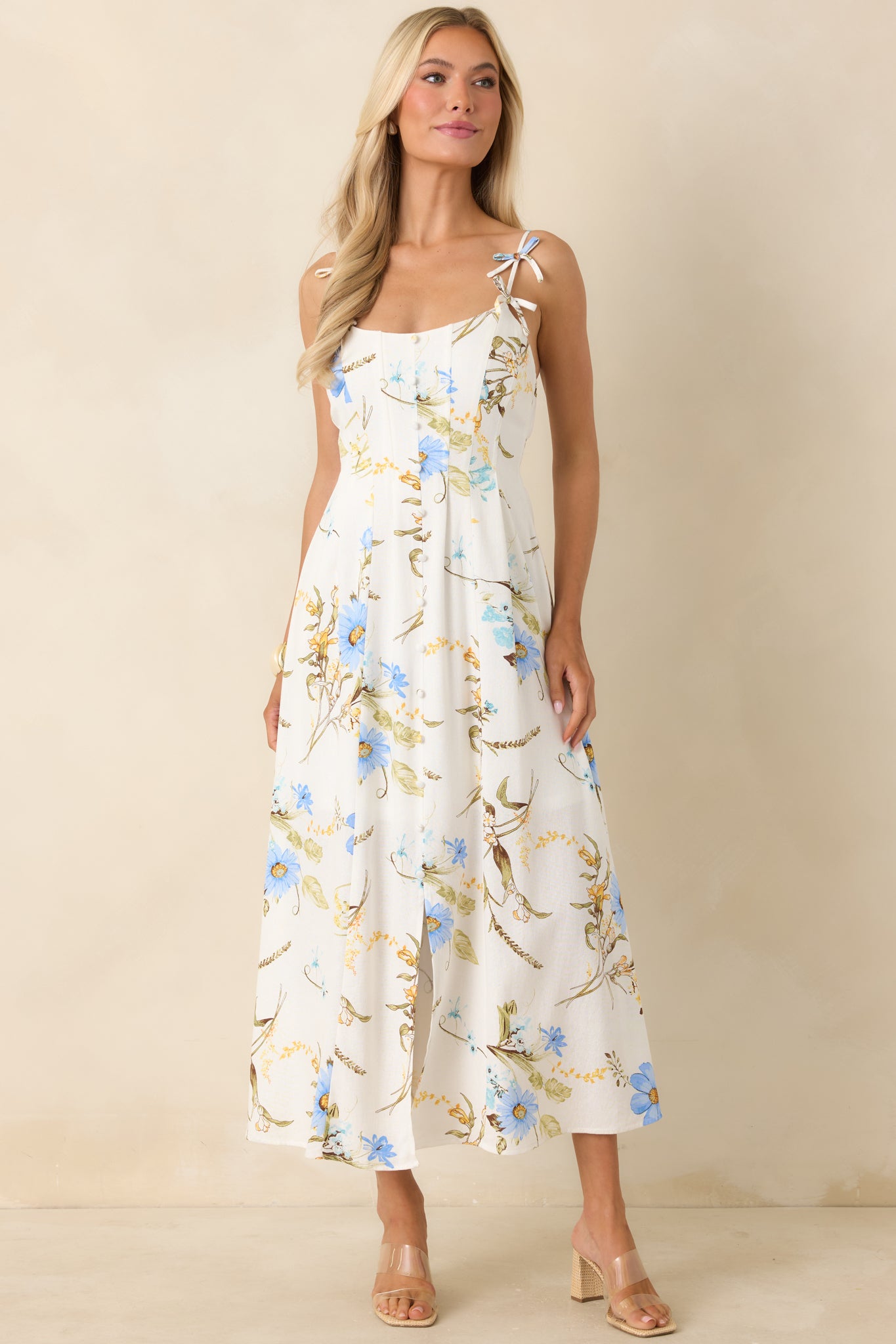Blue floral midi dress with bow-accent straps, structured bodice seams, and a lightweight, softly flared hemline.
