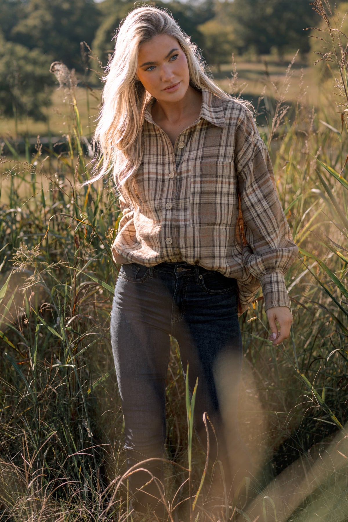 Woman modeling a beige flannel shirt with dark skinny jeans in a field of grass.