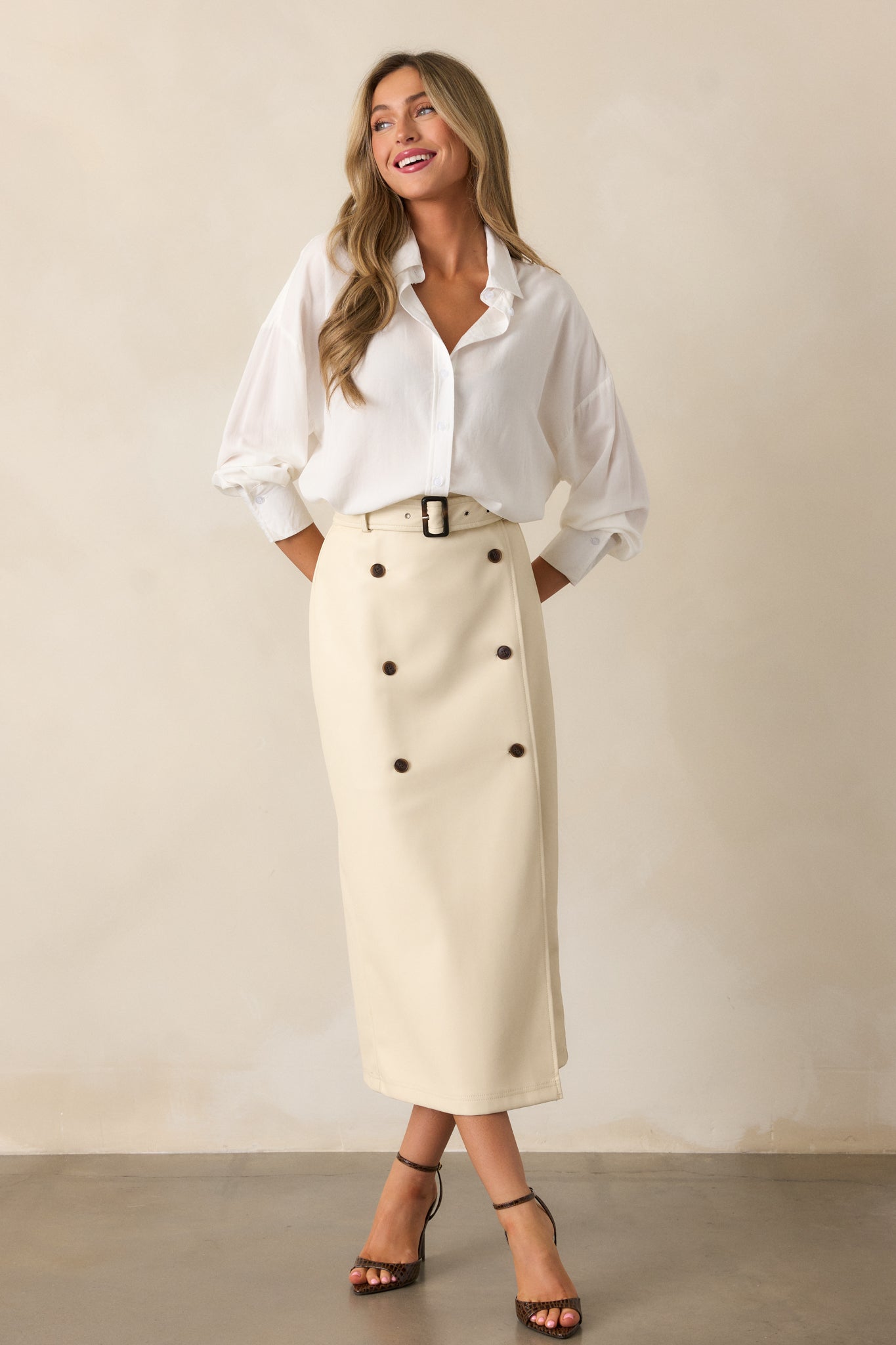 A chic ecru midi skirt in a high-waisted silhouette, accented with a belt, front buttons, and a side slit that enhances the flowy design.