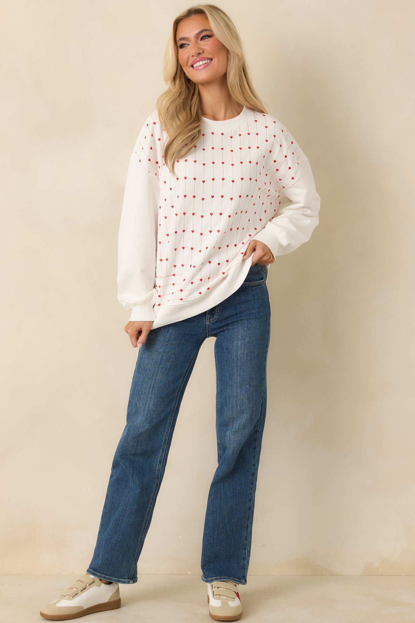 Relaxed white cotton crewneck sweatshirt featuring continuous vertical lines of embroidered hearts across the entire front, framed by ribbed cuffs and hem.