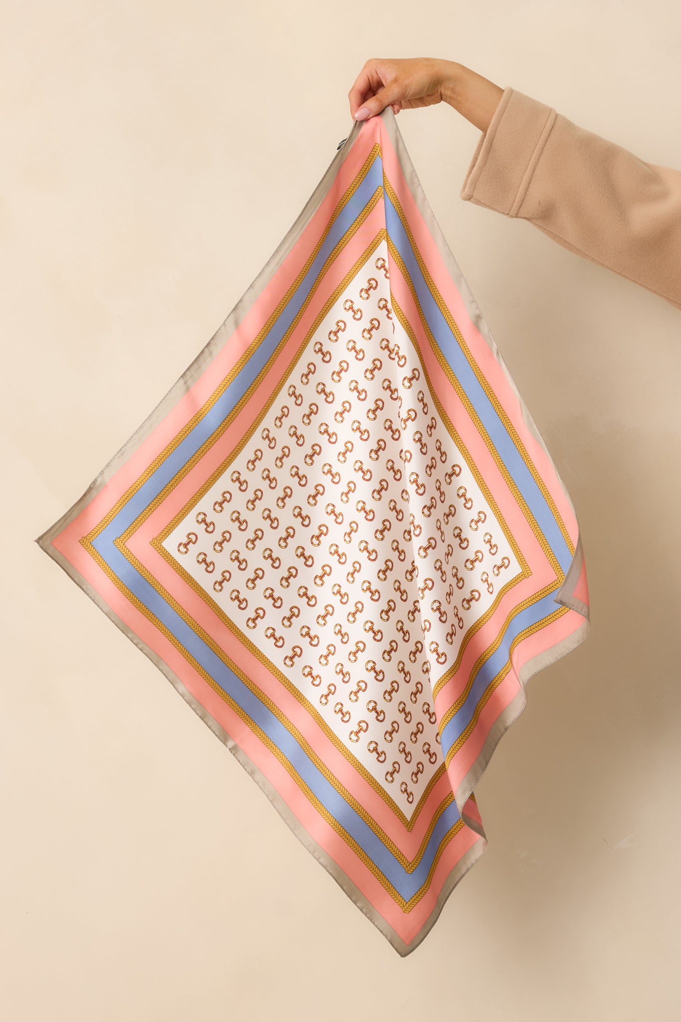 Alternate full view of the square pink scarf showcasing the gold snaffle motif and pink, gold, and periwinkle chain border.