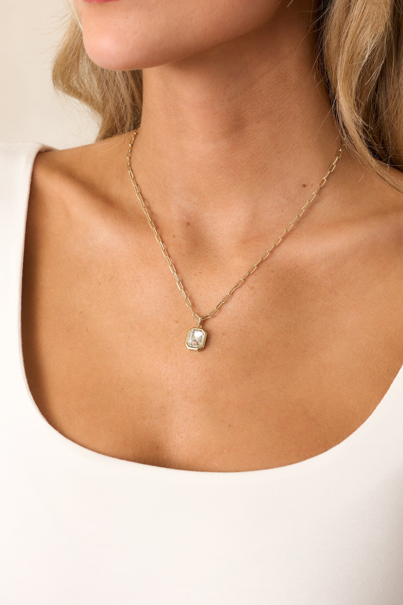 This gold necklace showcases a simple yet sophisticated rectangular chain with a square gold-bordered rhinestone pendant, secured with a lobster claw closure for easy wear.