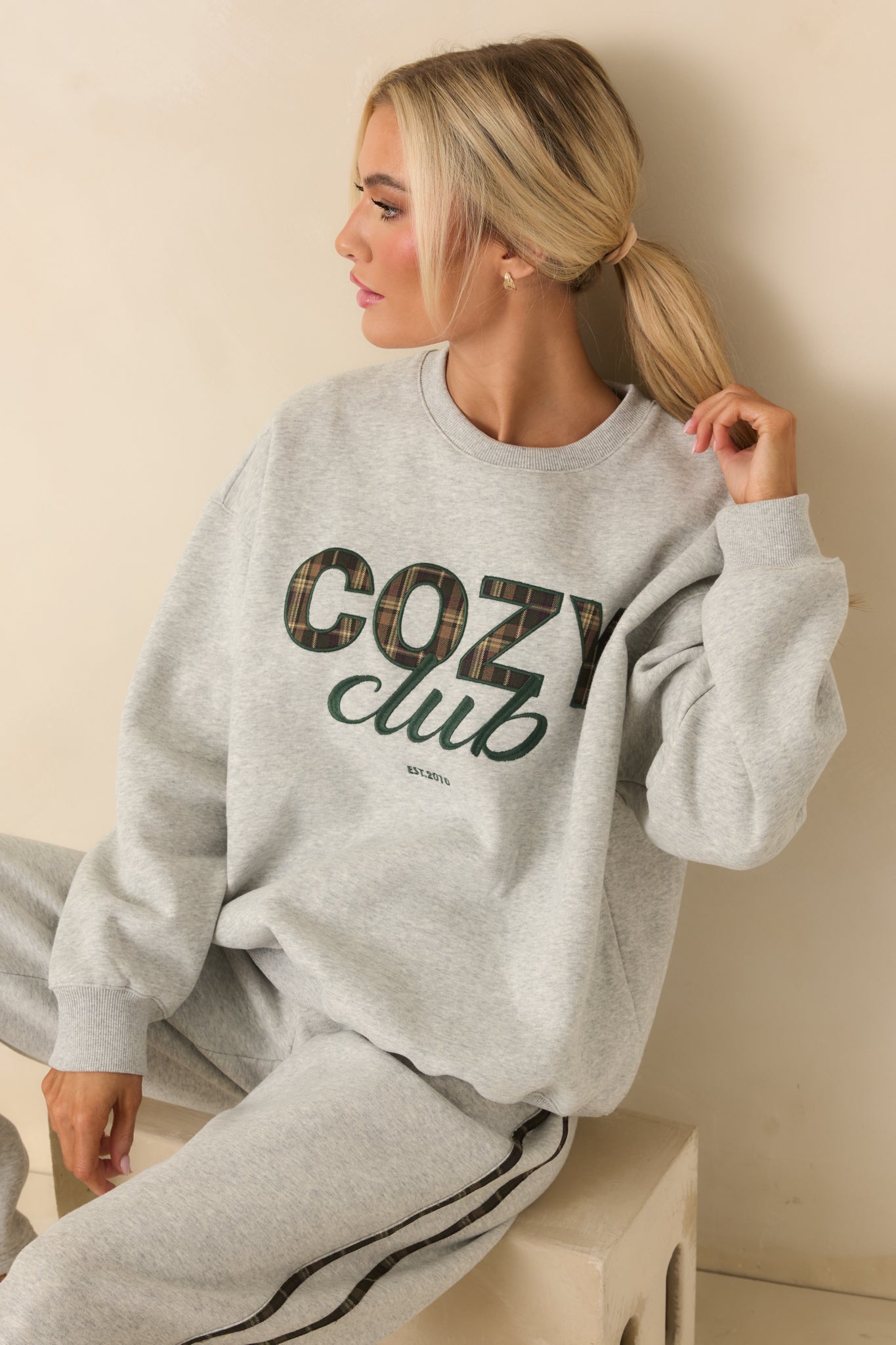 Cropped view highlighting plaid “Cozy Club” graphic and soft knit texture of grey sweatshirt.