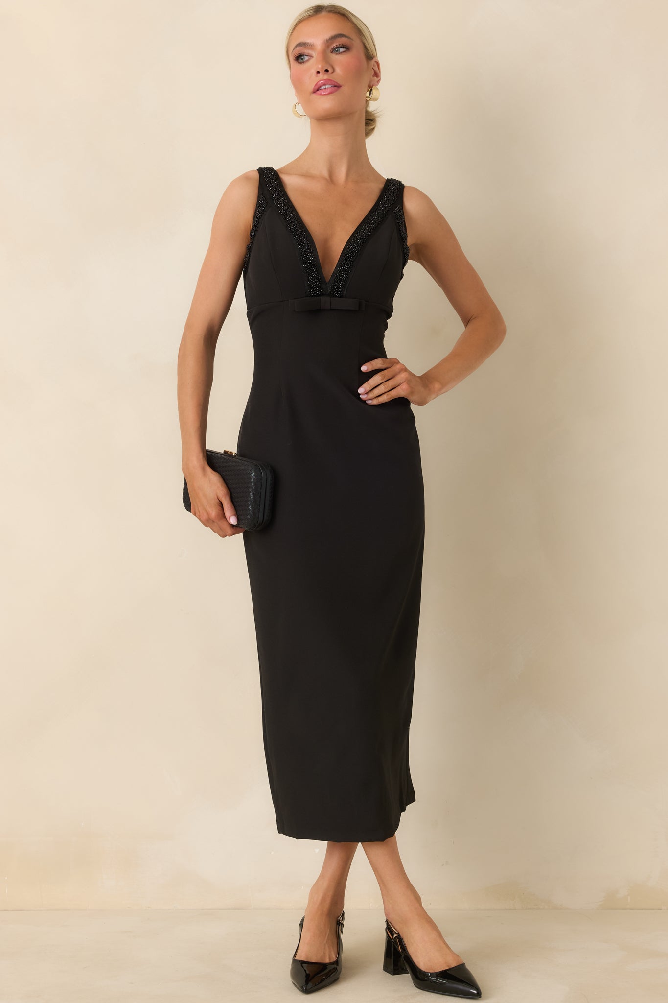 Front view of black midi dress featuring a fitted bodice, seam detailing, and small bow accent under the bust.