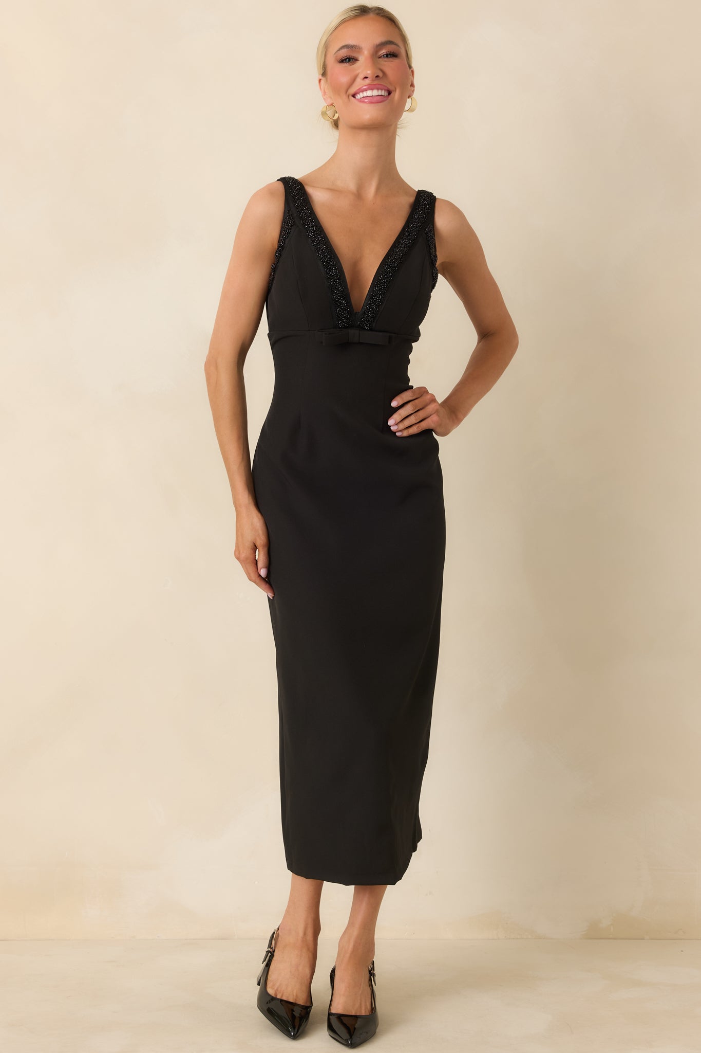 Black midi dress with V-neckline, fitted bodice, small under-bust bow, and back slit for ease of movement.
