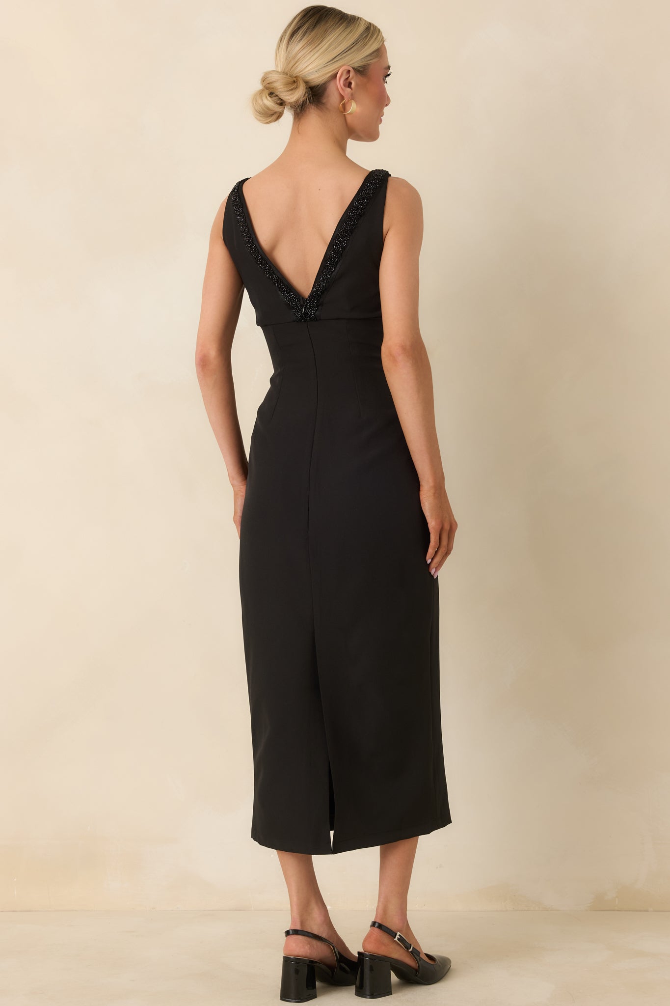 Rear view of black midi dress highlighting back tonal beading and slit, with smooth, structured fabric finish.