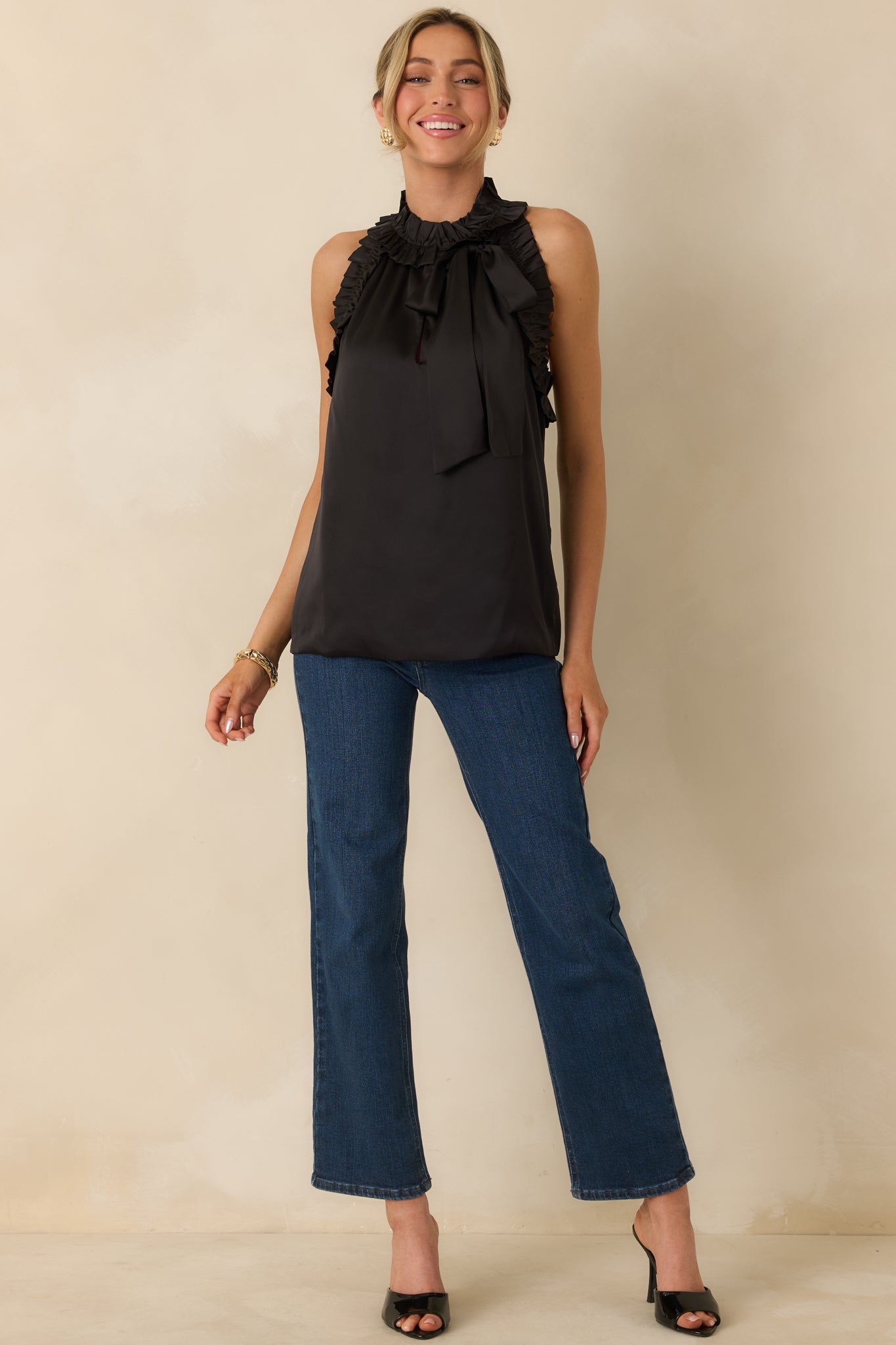 Black sleeveless top with a soft drape, ruffled neckline, and front bow closure for added detail.