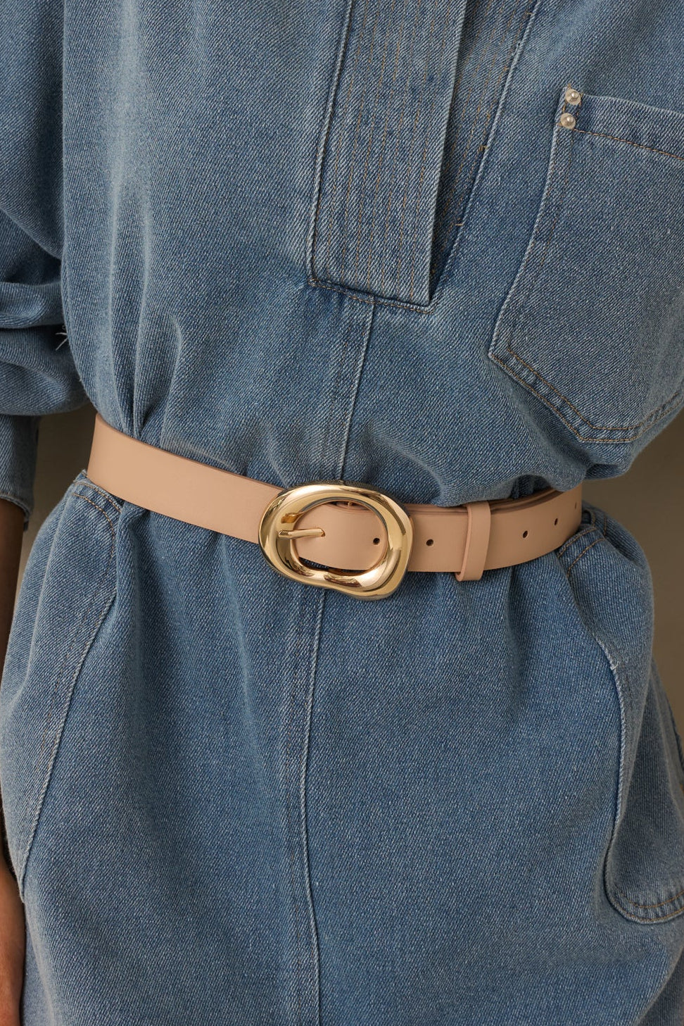 Close-up of taupe belt highlighting hollow gold buckle, faux leather texture, and pin closure.