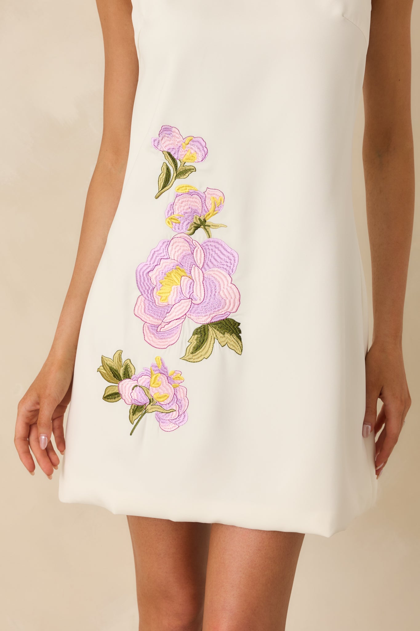 Detailed look at lavender and pink floral embroidery threads on ivory woven base.