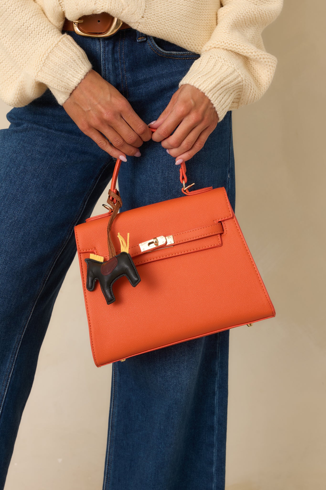 Cropped front angle showing the twist lock closure and dual overlapping straps on the orange handbag flap.