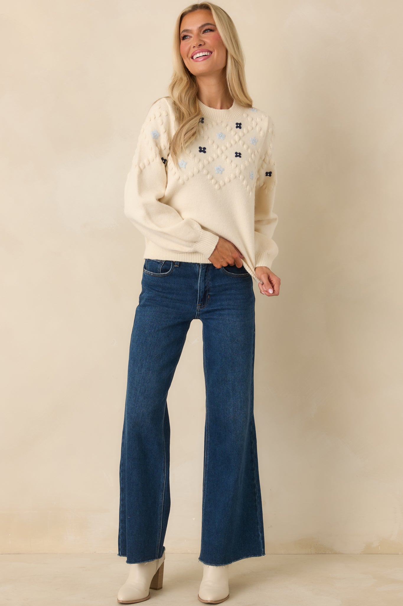 Ivory knit sweater with raised bobble texture and colorful floral embroidery across the front, finished with a classic crew neckline.