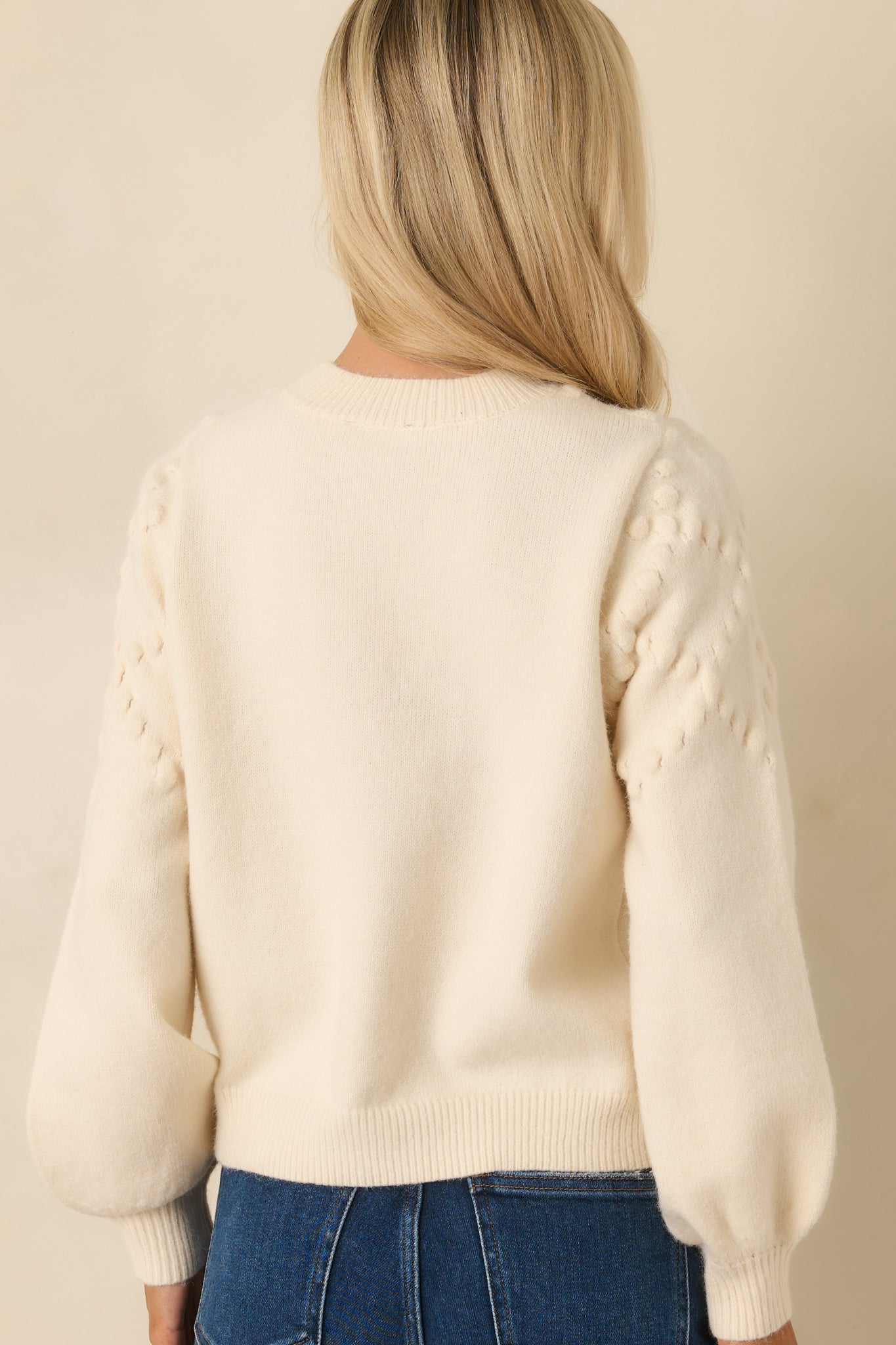 Rear view of the ivory knit sweater displaying the bobble-textured fabric, long sleeves, and ribbed hem and cuffs without embroidery.