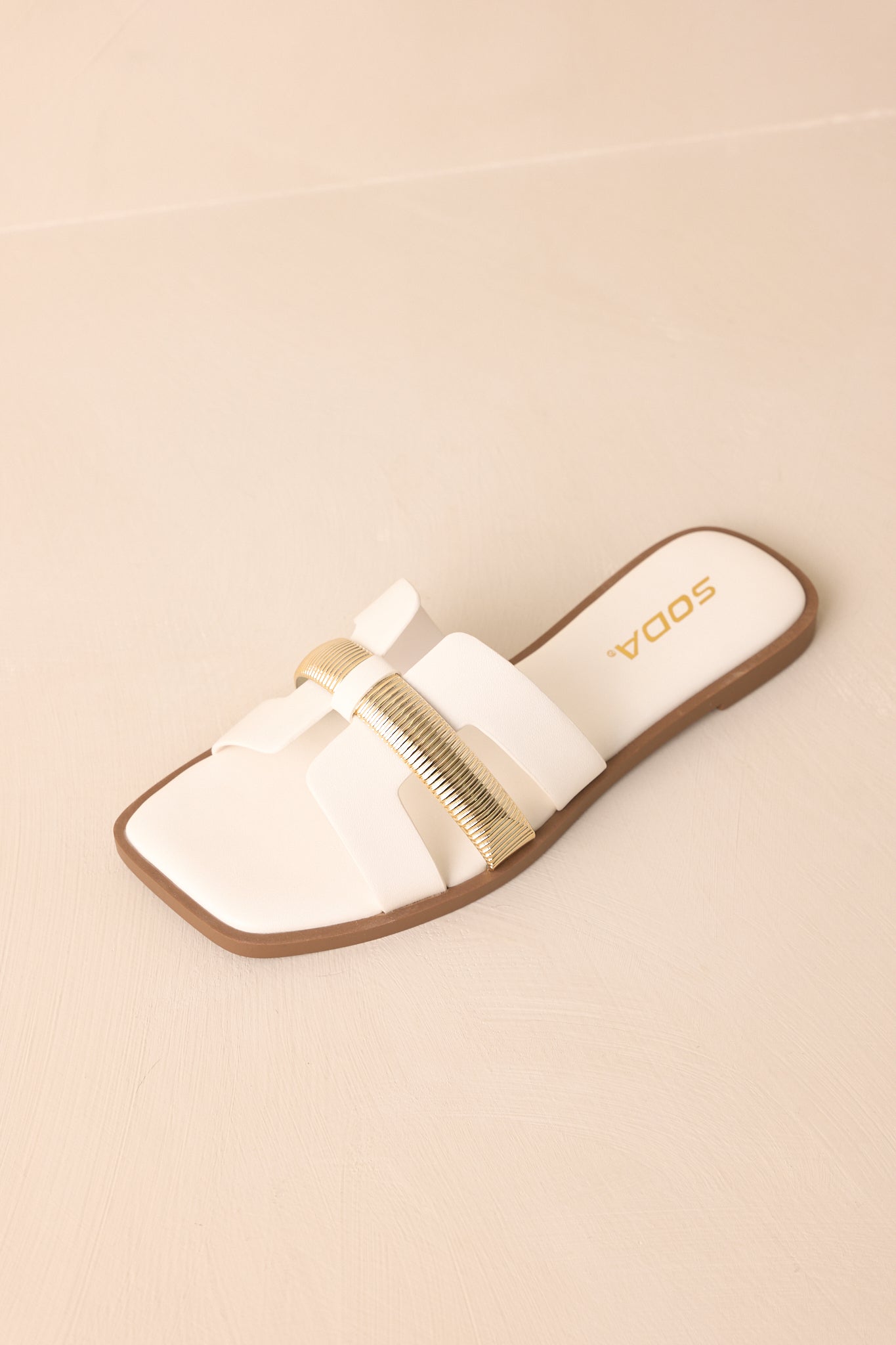 Overhead view of the white sandals against a beige background, showing the full slide-on silhouette.