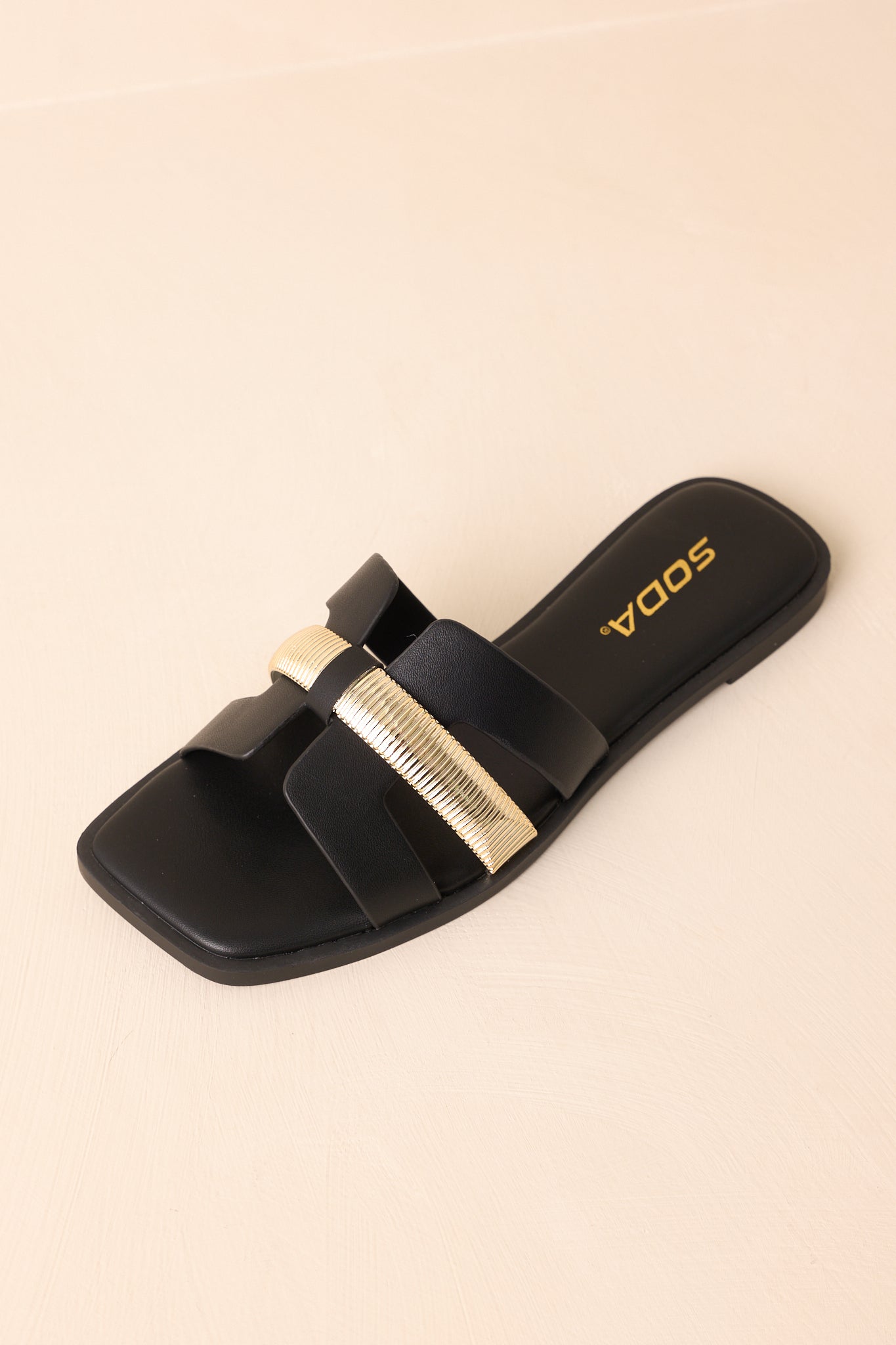 Overhead view of the black sandals against a beige background, showing the full slide-on silhouette.