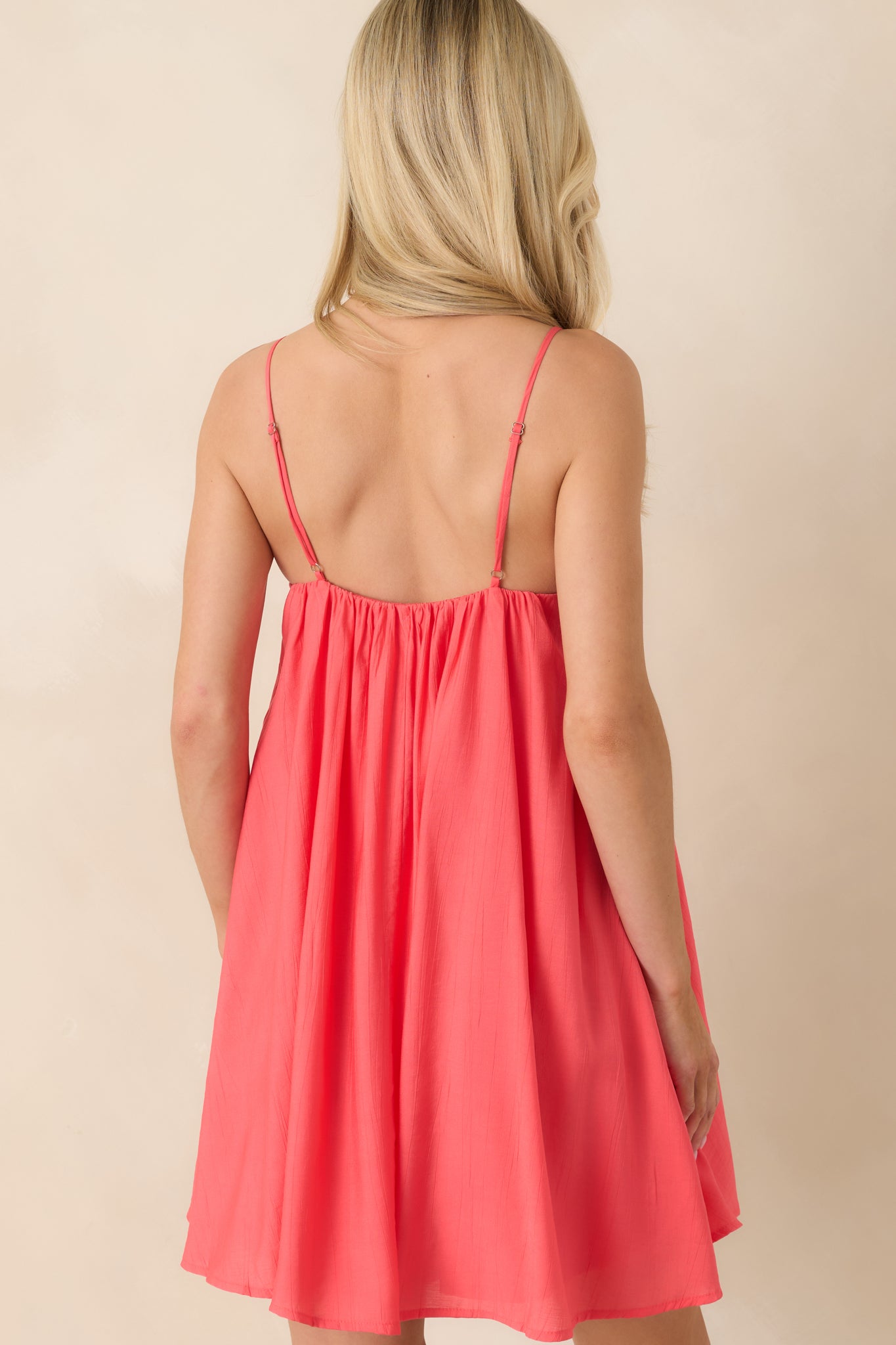 Coral pink mini dress with adjustable straps and softly gathered rear silhouette.