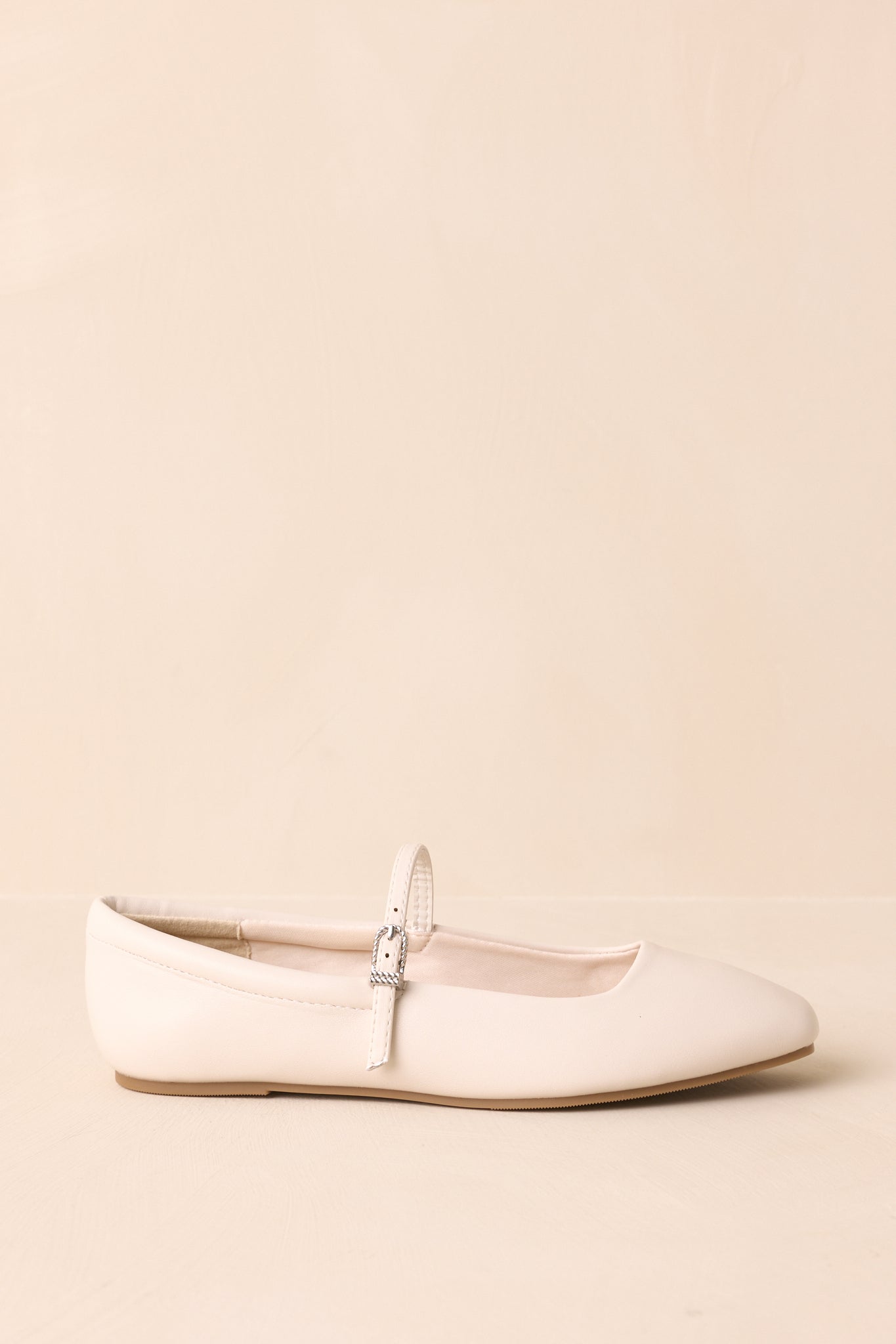 A detailed side view of the adjustable silver buckle on the mary jane strap of the ivory flat.
