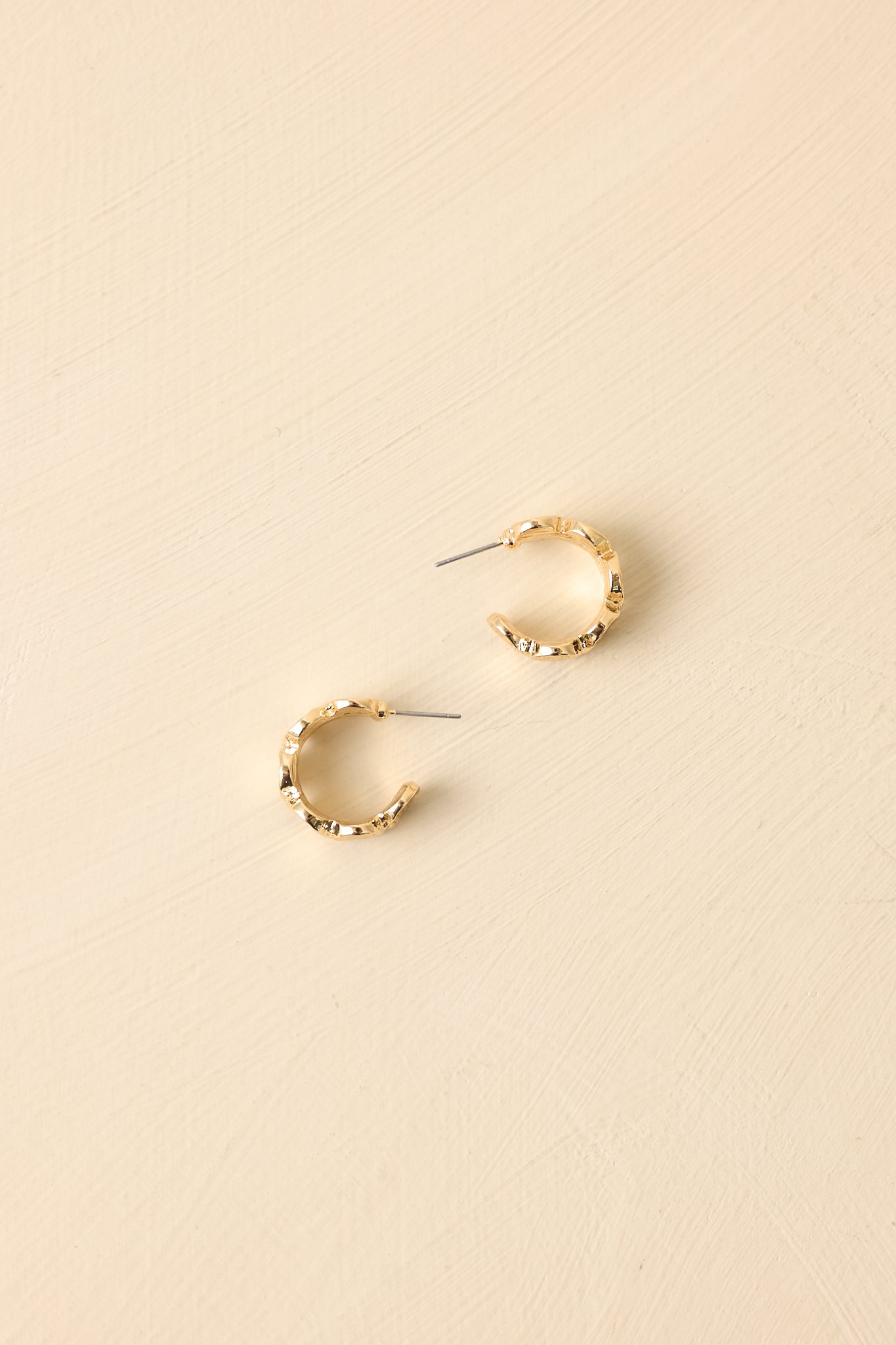 Front view of gold hoop earrings displayed on beige background emphasizing organic circular design.