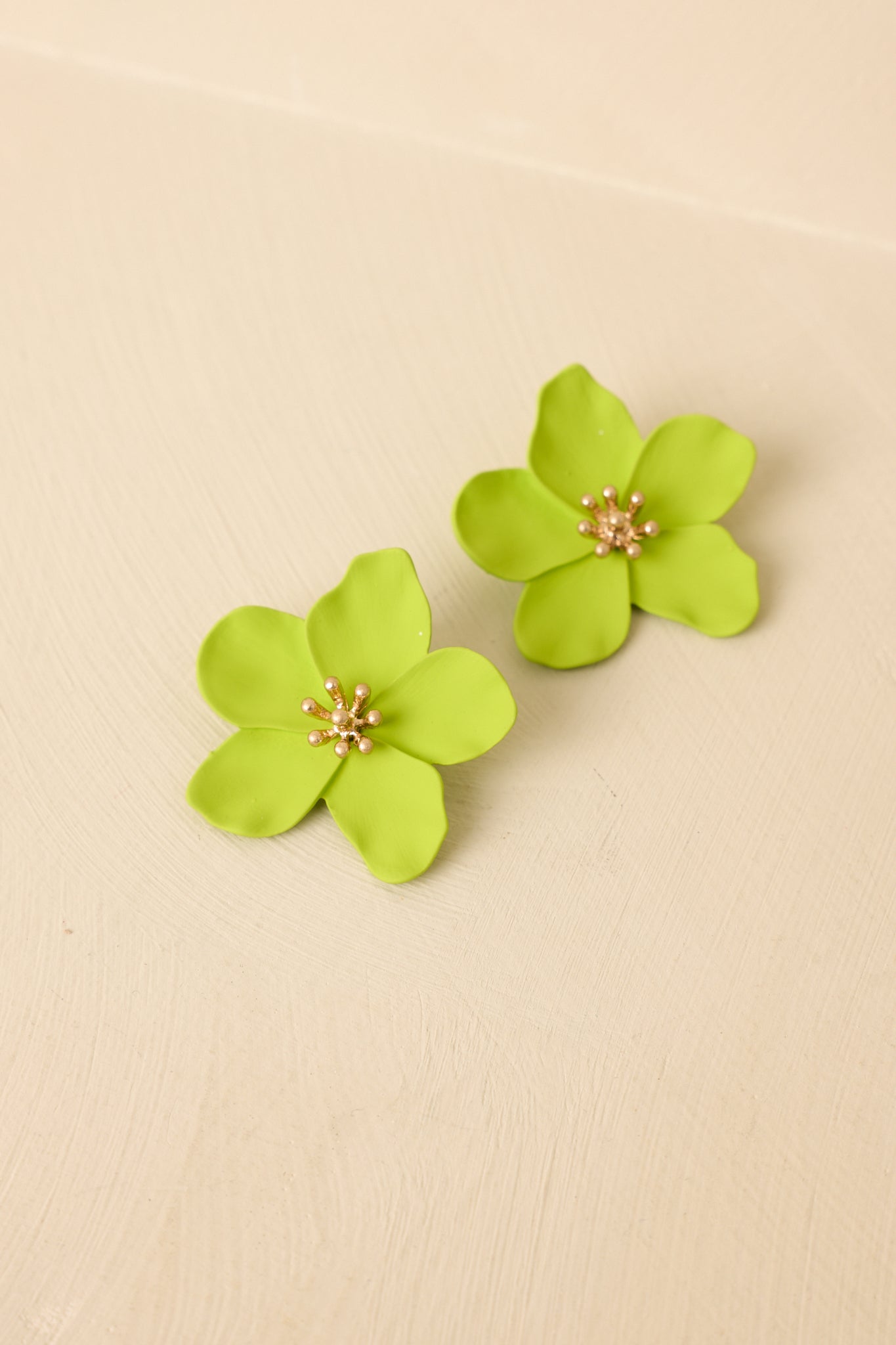 Front view of green floral earrings displayed on beige background emphasizing oversized shape and shine.