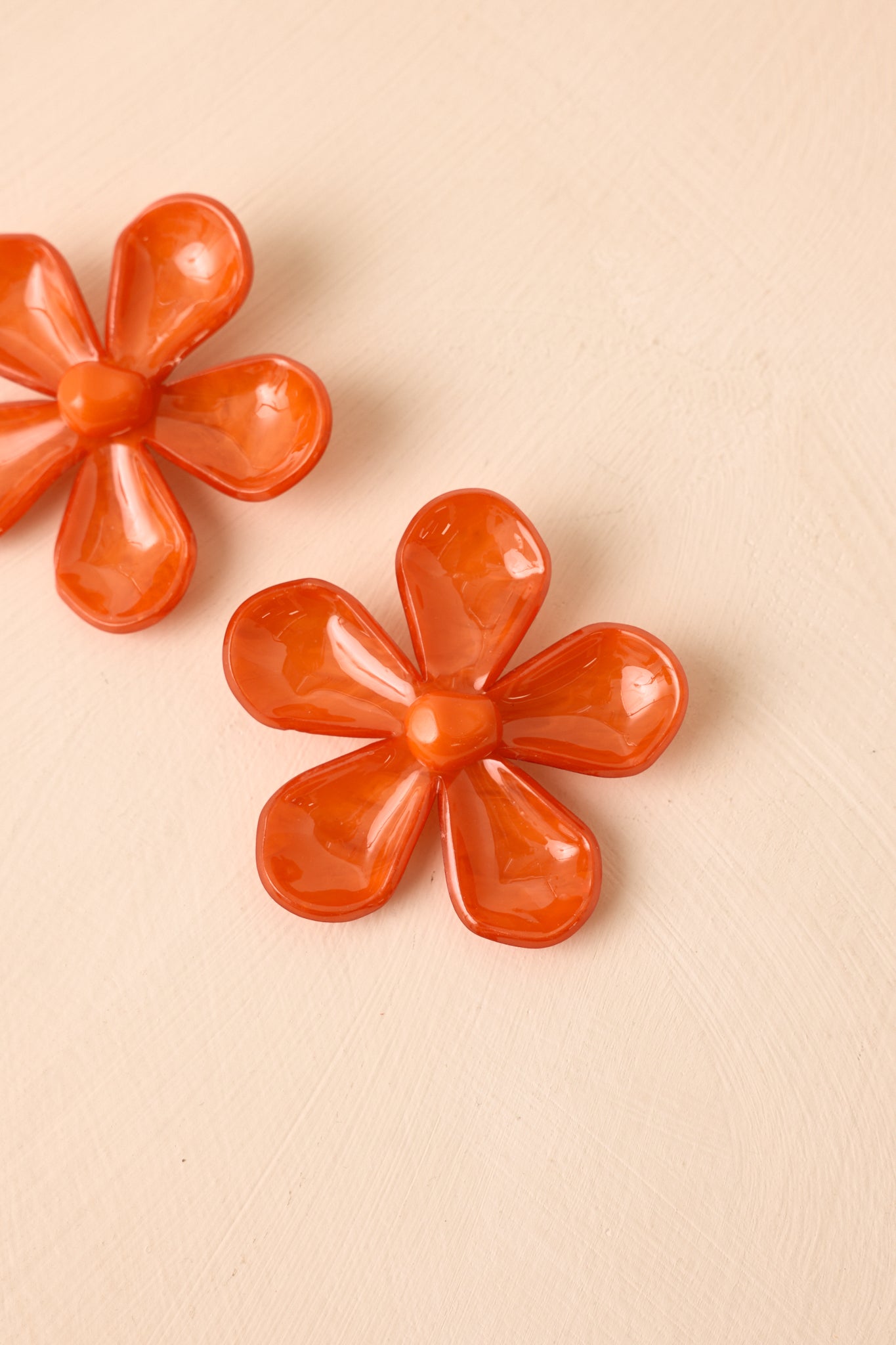 Angled view of glossy floral earrings on beige backdrop highlighting dimensional petals and vibrant color.